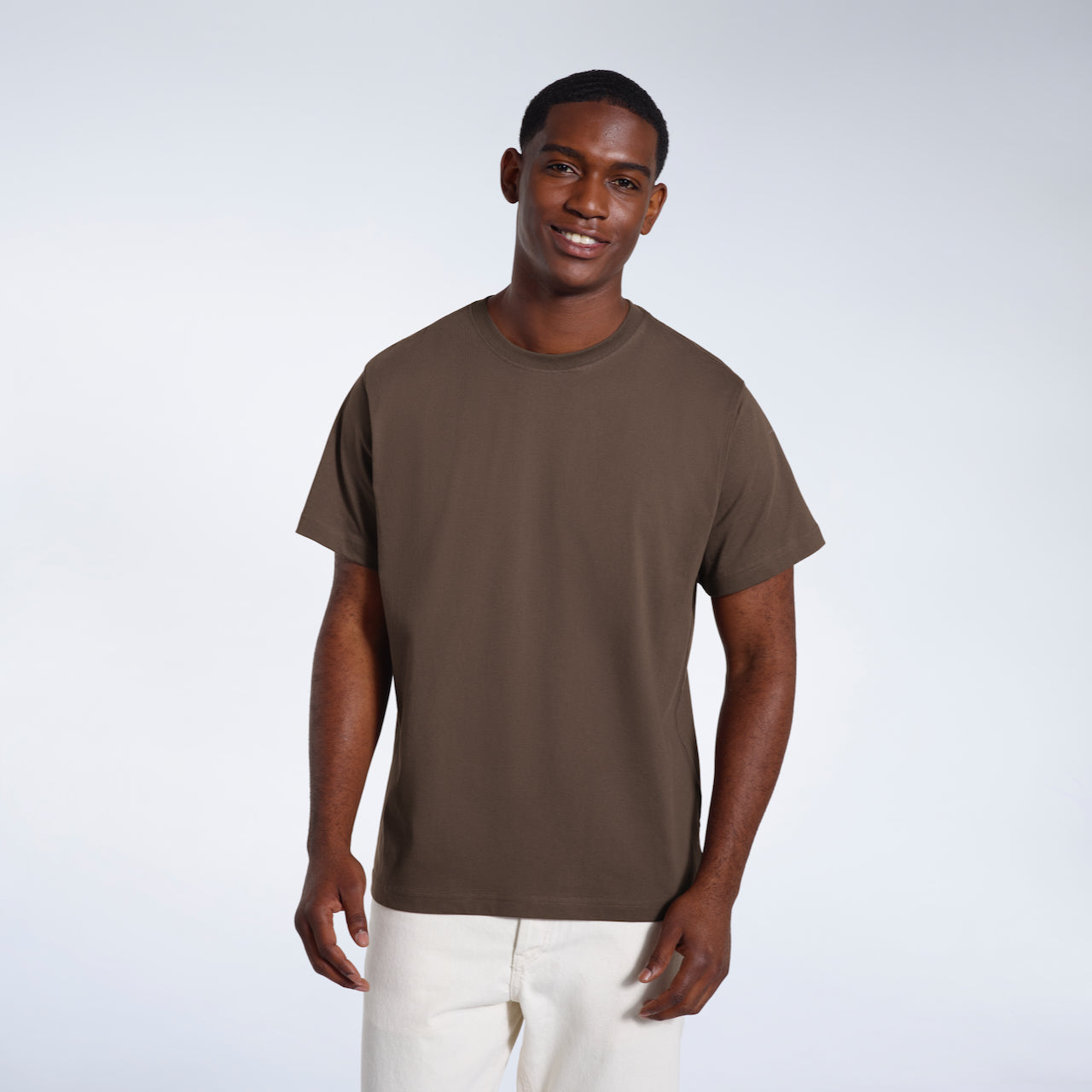 A man smiling looking into the camera, modelling a plain dark khaki short sleeve organic cotton t shirt.