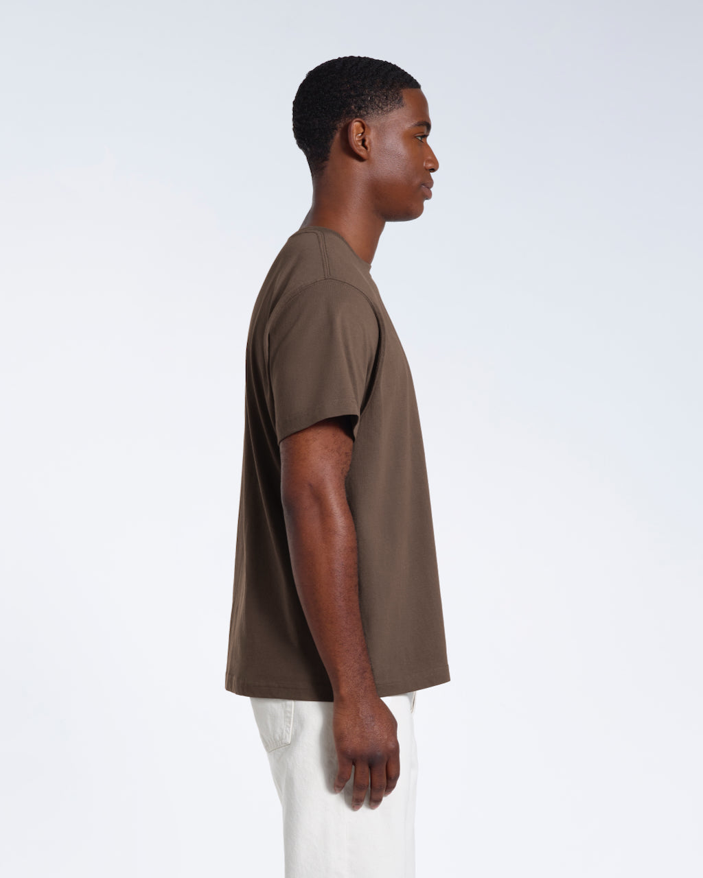 A man facing side on, modelling a plain dark khaki short sleeve organic cotton t shirt.