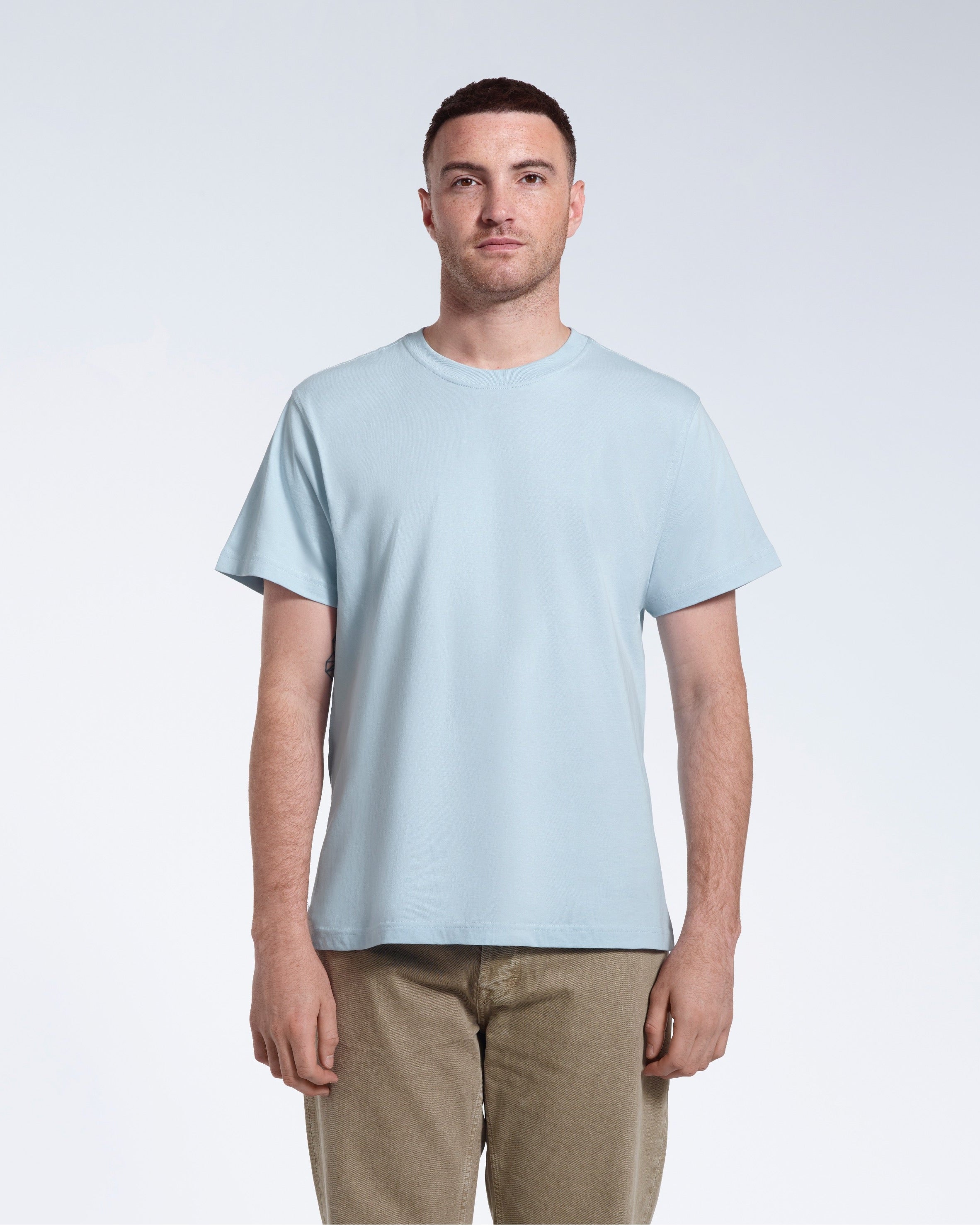 A man facing front on looking into the camera, modelling a plain light blue short sleeve organic cotton t shirt.