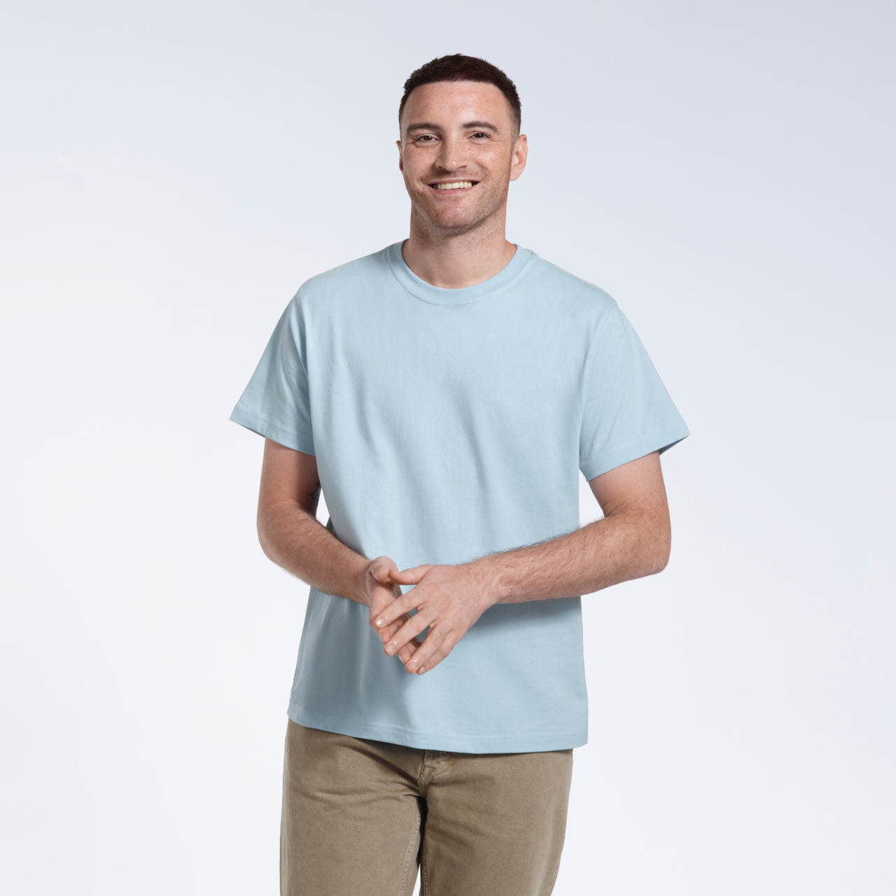 A man smiling into the camera with his hands together, modelling a plain light blue short sleeve organic cotton t shirt.