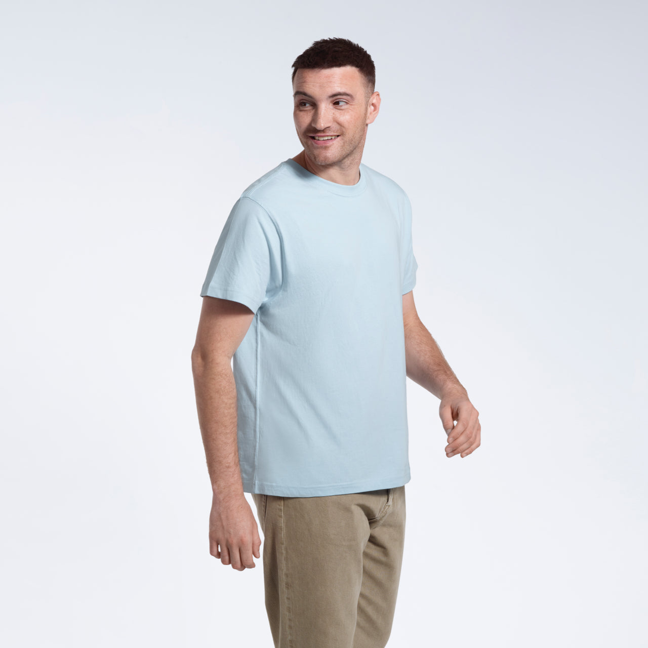 A man smiling looking back, modelling a plain light blue short sleeve organic cotton t shirt.