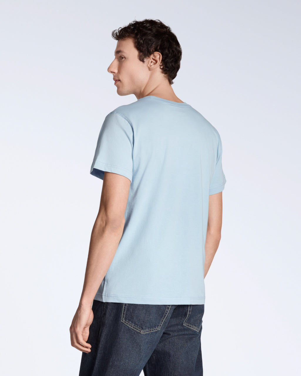 A man facing away from the camera, modelling a plain light blue short sleeve organic cotton t shirt.