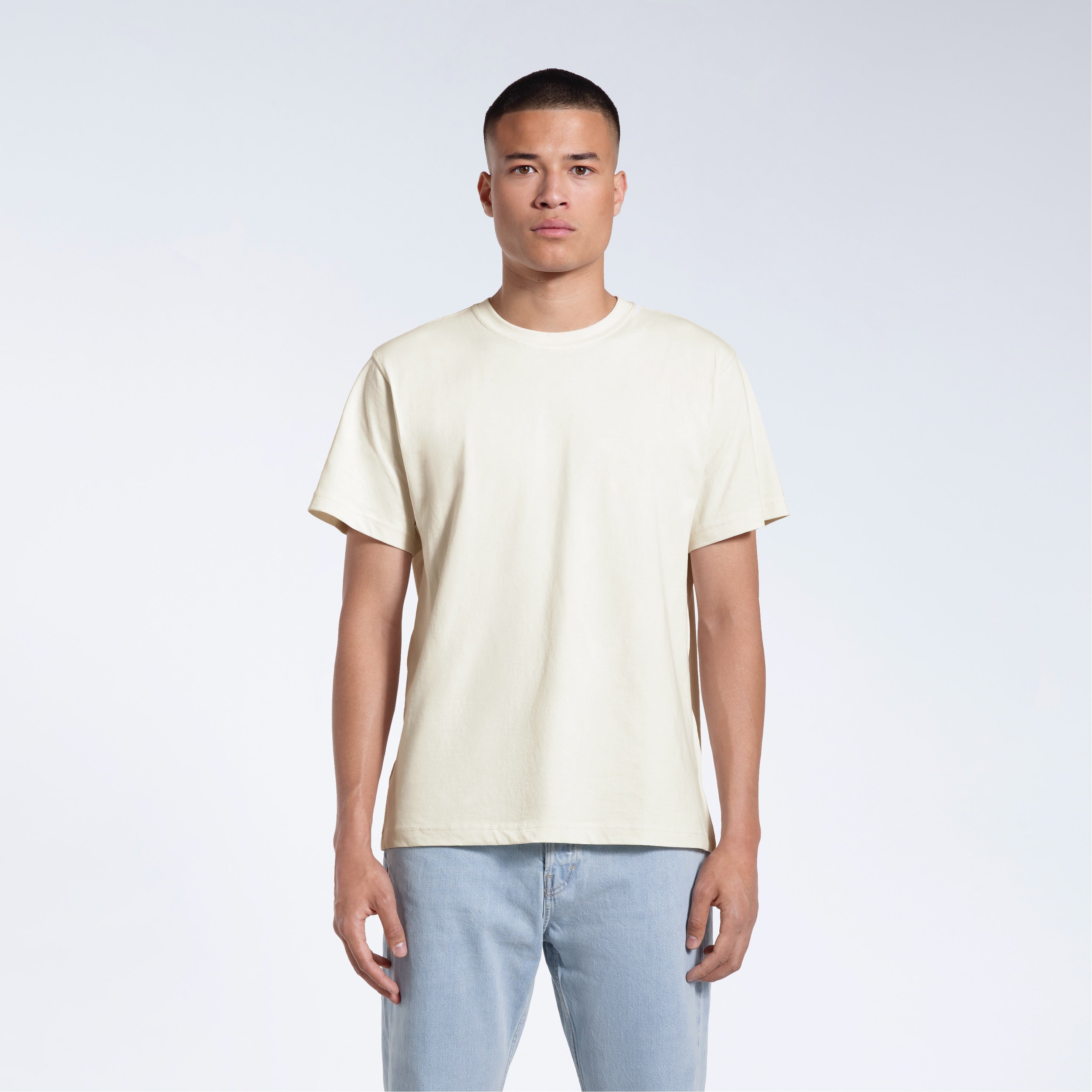 A man facing front on looking into the camera, modelling a plain ecru short sleeve organic cotton t shirt.
