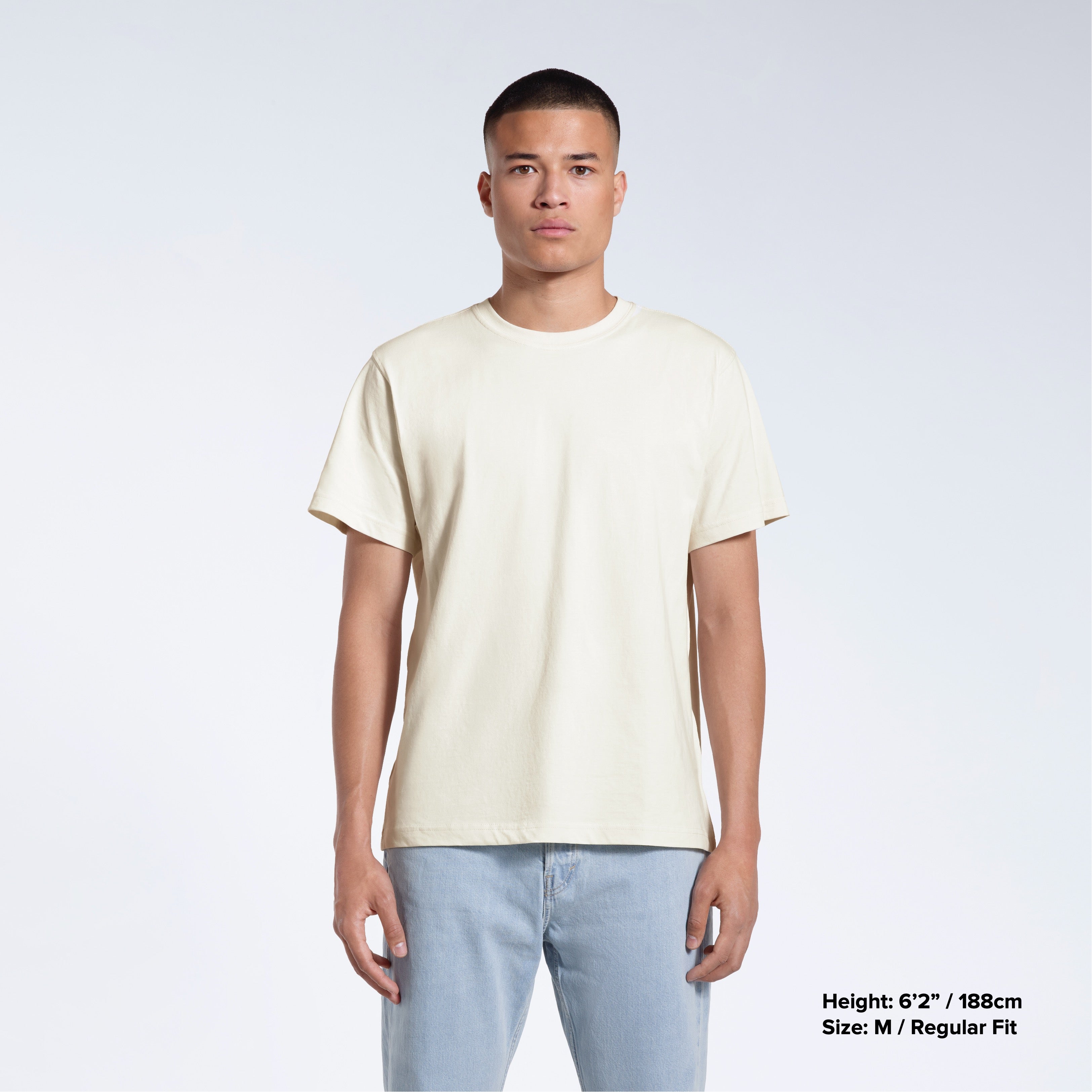 A man facing front on looking into the camera, modelling a plain ecru short sleeve organic cotton t shirt.