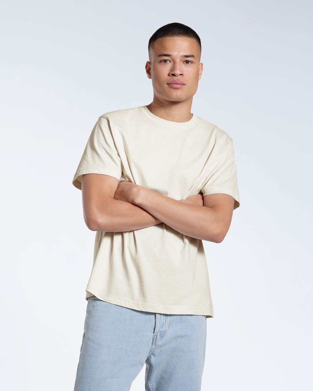 A man looking into the camera with his arms crossed, modelling a plain ecru short sleeve organic cotton t shirt.