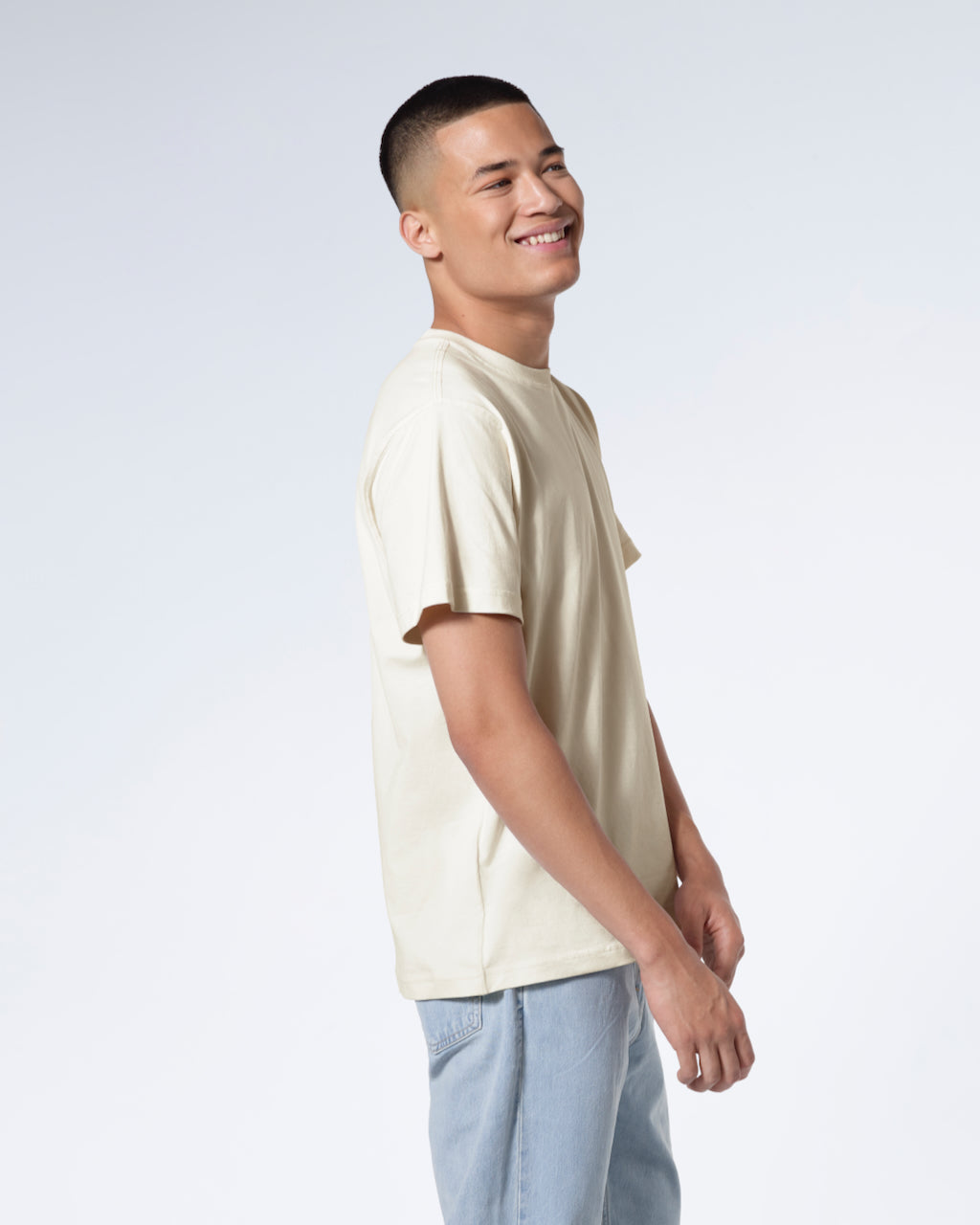 A man facing side on smiling, modelling a plain ecru short sleeve organic cotton t shirt.