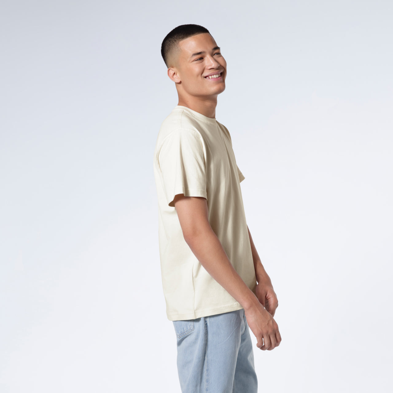 A man facing side on smiling, modelling a plain ecru short sleeve organic cotton t shirt.