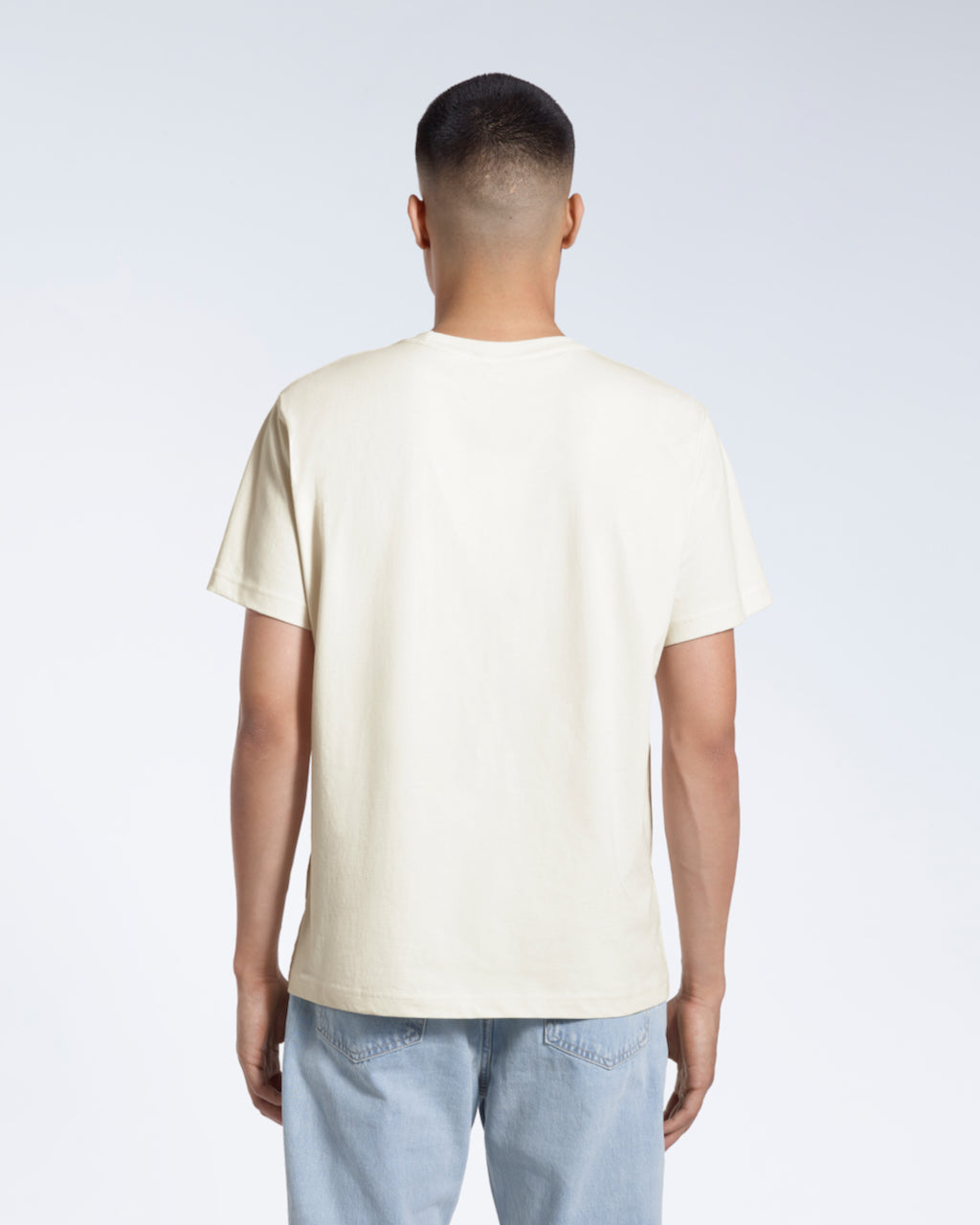 A man facing away from the camera, modelling a plain ecru short sleeve organic cotton t shirt.