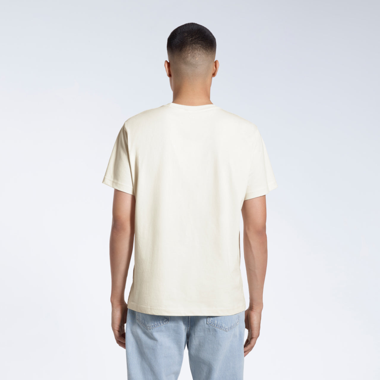 A man facing away from the camera, modelling a plain ecru short sleeve organic cotton t shirt.