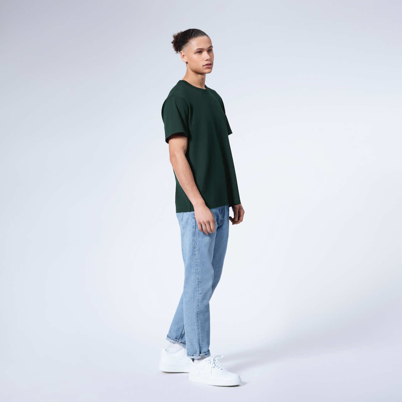 A full body photo of a man with his arms by his sides, modelling a plain green short sleeve organic cotton t shirt.