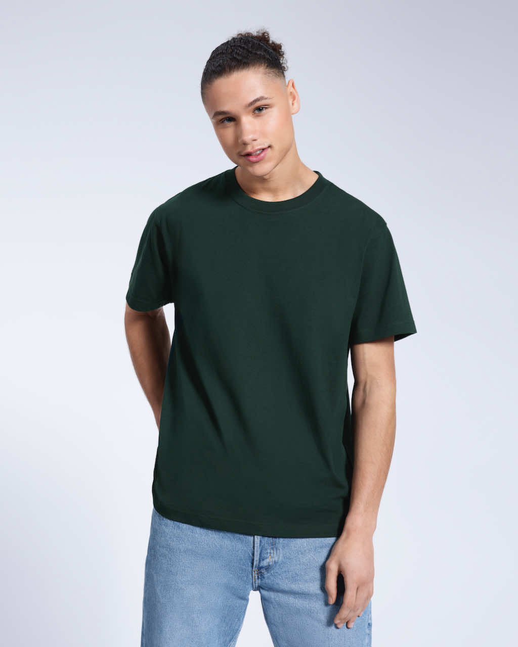 A man smiling into the camera with one hand in his back pocket, modelling a plain green short sleeve organic cotton t shirt.