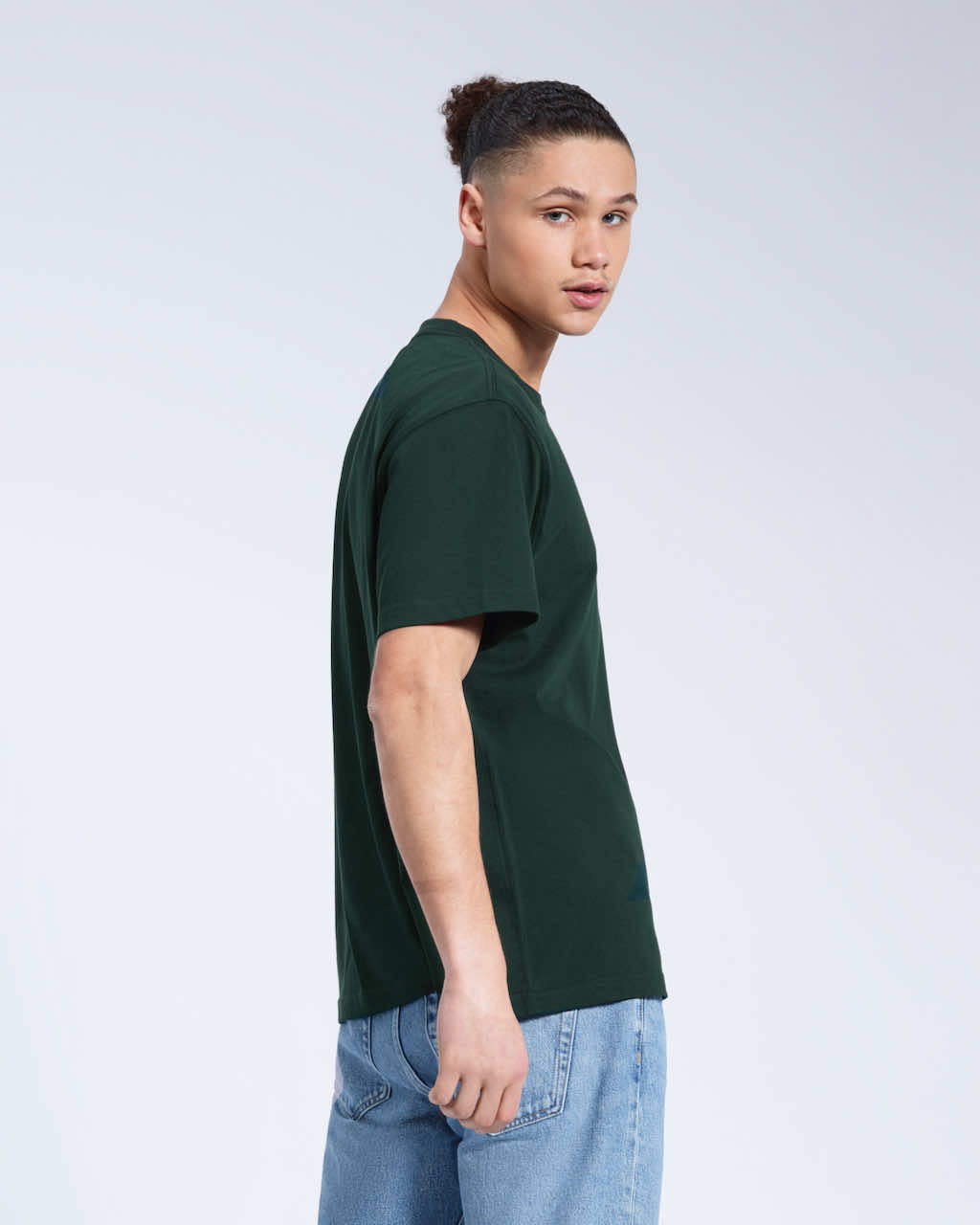 A man looking back towards the camera, modelling a plain green short sleeve organic cotton t shirt.