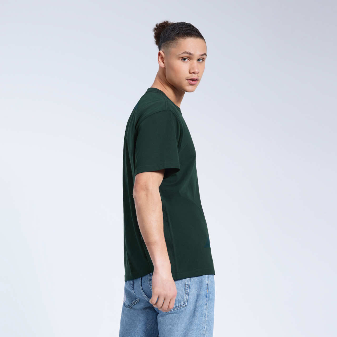 A man looking back towards the camera, modelling a plain green short sleeve organic cotton t shirt.