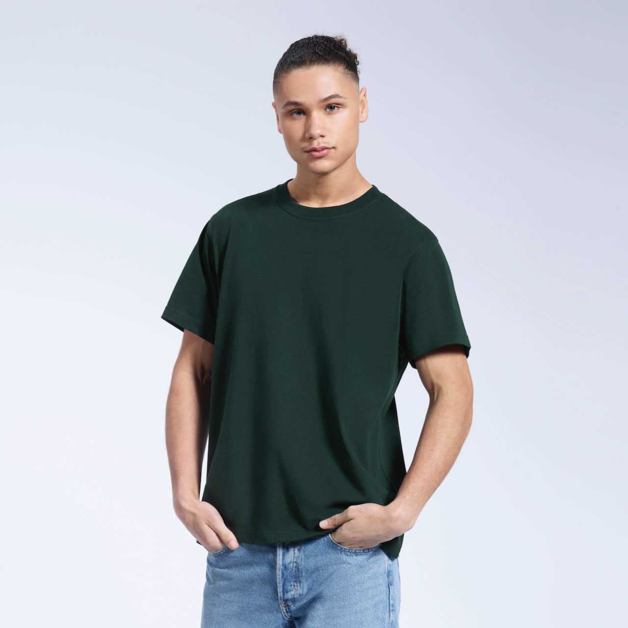 A man with his hands in his pockets, modelling a plain green short sleeve organic cotton t shirt.