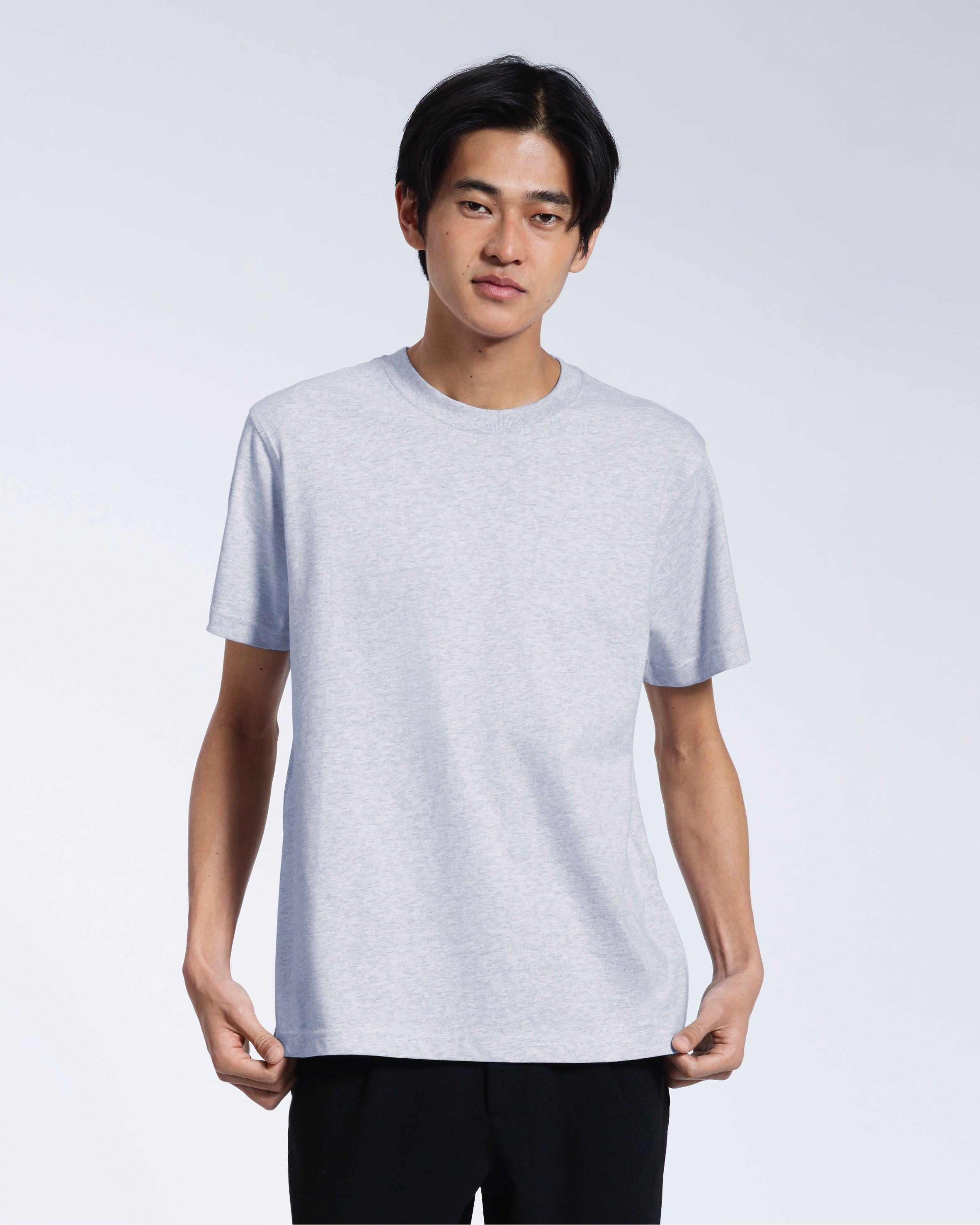 A man looking into the camera, touching the bottom of his plain grey short sleeve organic cotton t shirt.