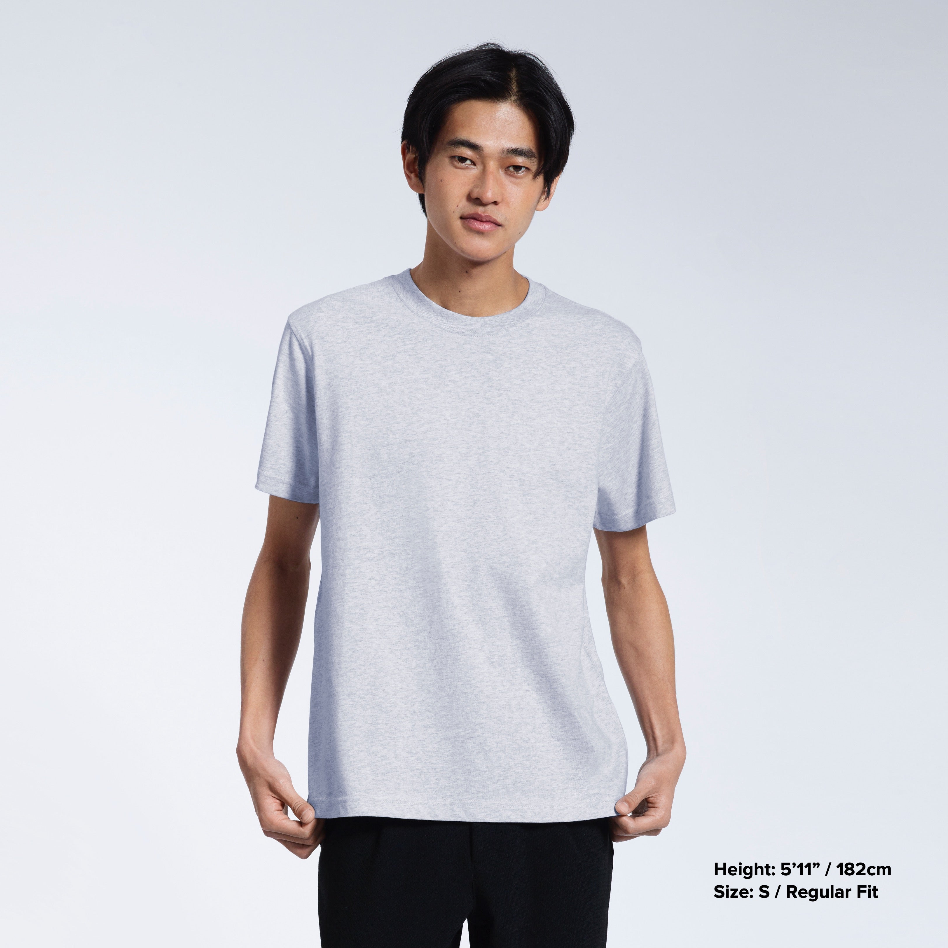 A man looking into the camera, touching the bottom of his plain grey short sleeve organic cotton t shirt.