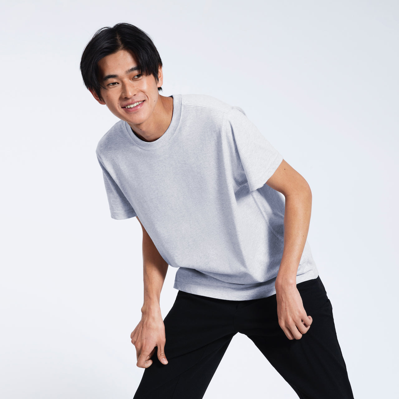 A man leaning over slightly, smiling, modelling a plain short sleeve grey organic cotton t shirt.