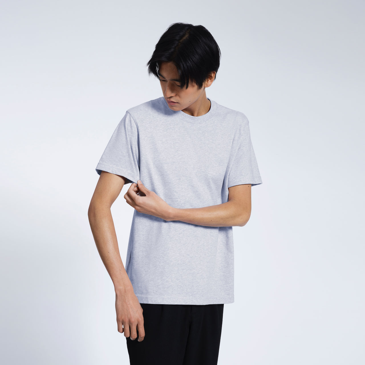 A man looking down touching his sleeve, modelling a plain grey short sleeve organic cotton t shirt.