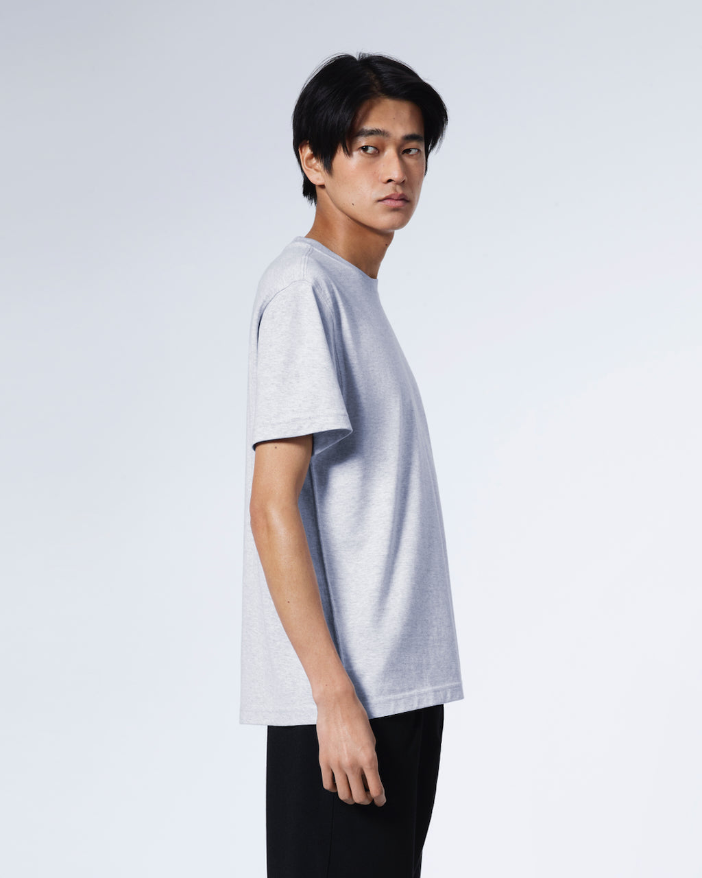 A man facing side on with his head turned towards the camera, modelling a plain grey short sleeve organic cotton t shirt.