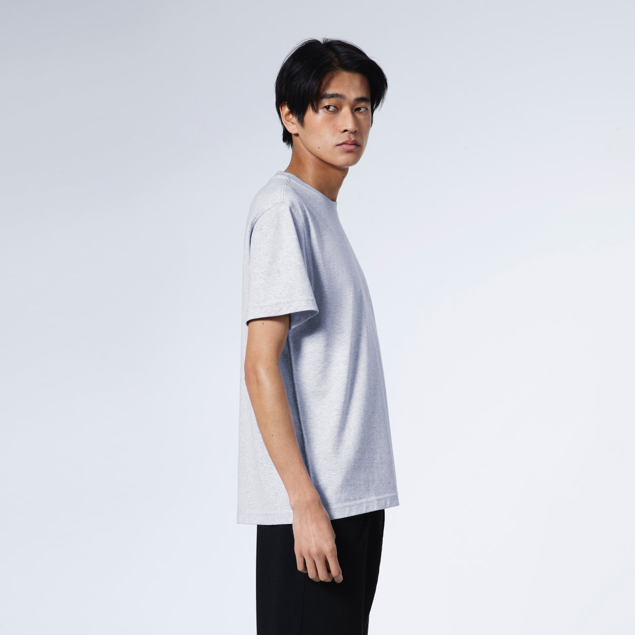 A man facing side on with his head turned towards the camera, modelling a plain grey short sleeve organic cotton t shirt.