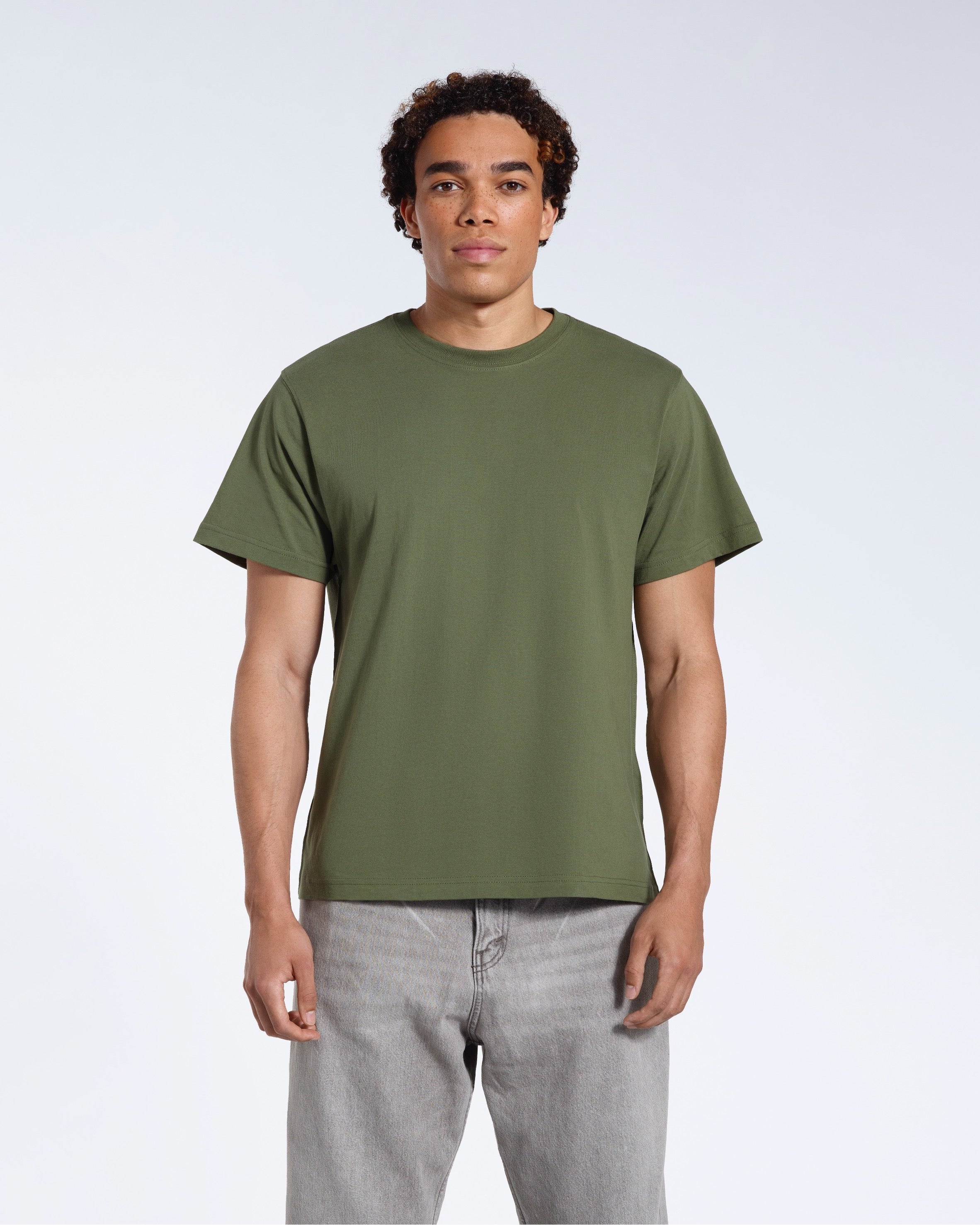 A man facing front on looking into the camera, modelling a plain khaki green short sleeve organic cotton t shirt.