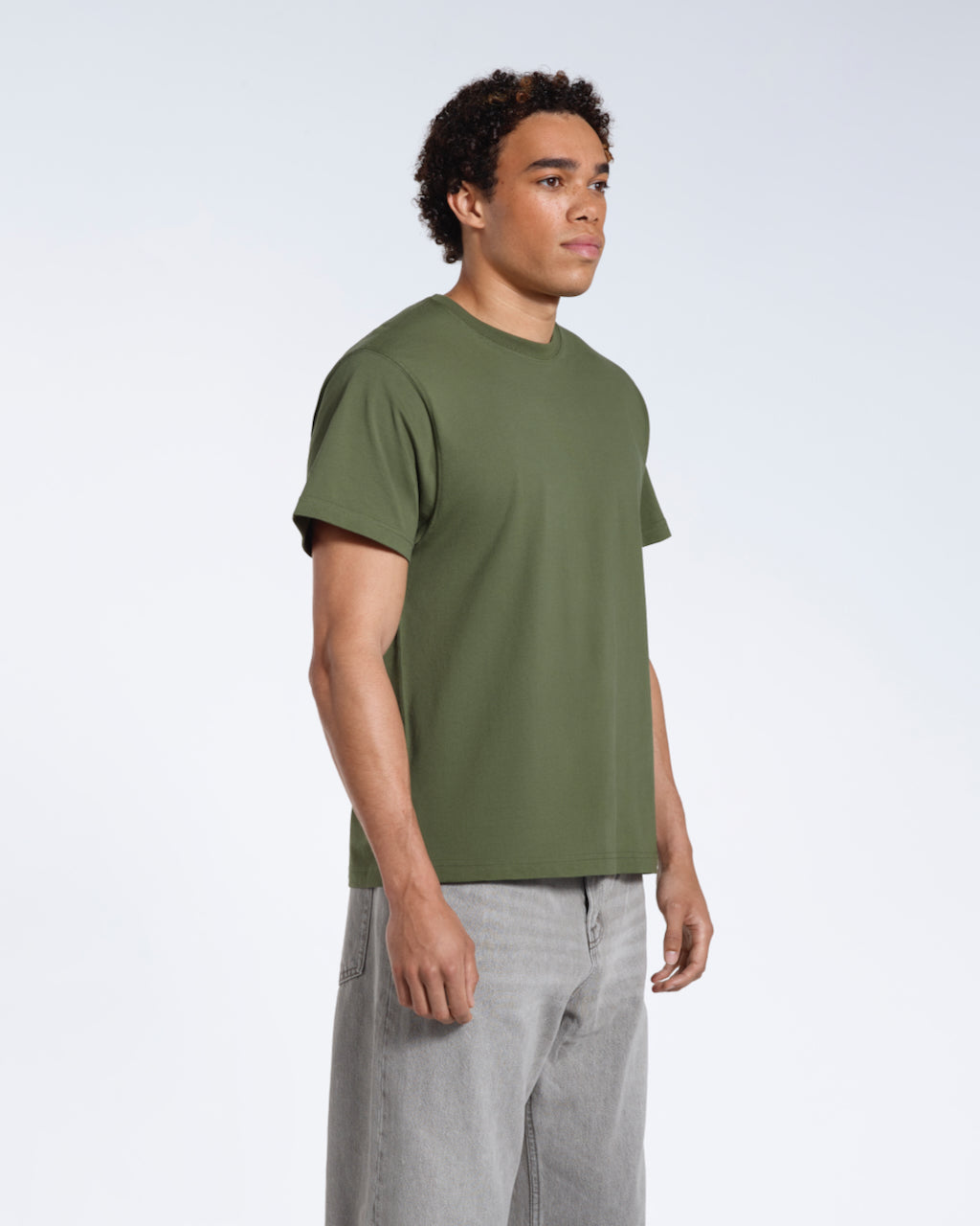 A man at an angle with his arms by his sides, modelling a plain khaki green short sleeve organic cotton t shirt.