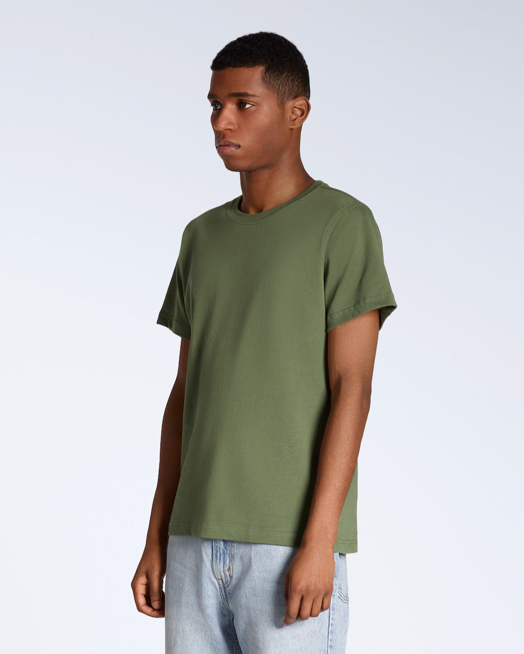 A man at an angle with his arms by his sides, modelling a plain khaki green short sleeve organic cotton t shirt.