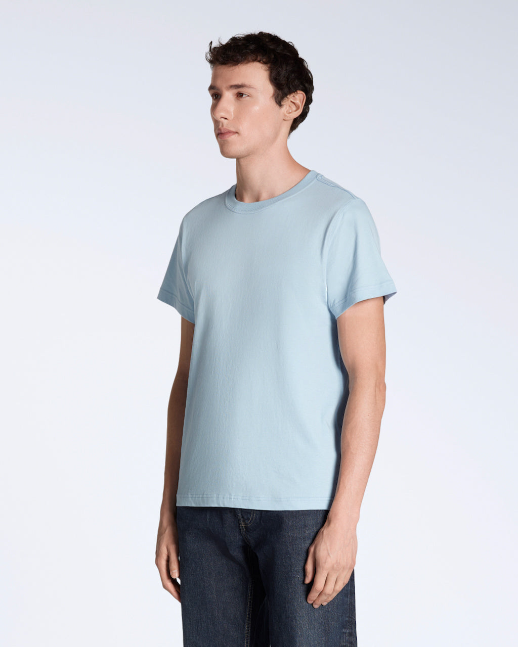 A man at an angle with his arms by his sides, modelling a plain light blue short sleeve organic cotton t shirt.