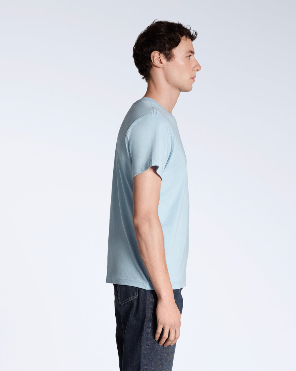 A man facing side on, modelling a plain light blue short sleeve organic cotton t shirt.