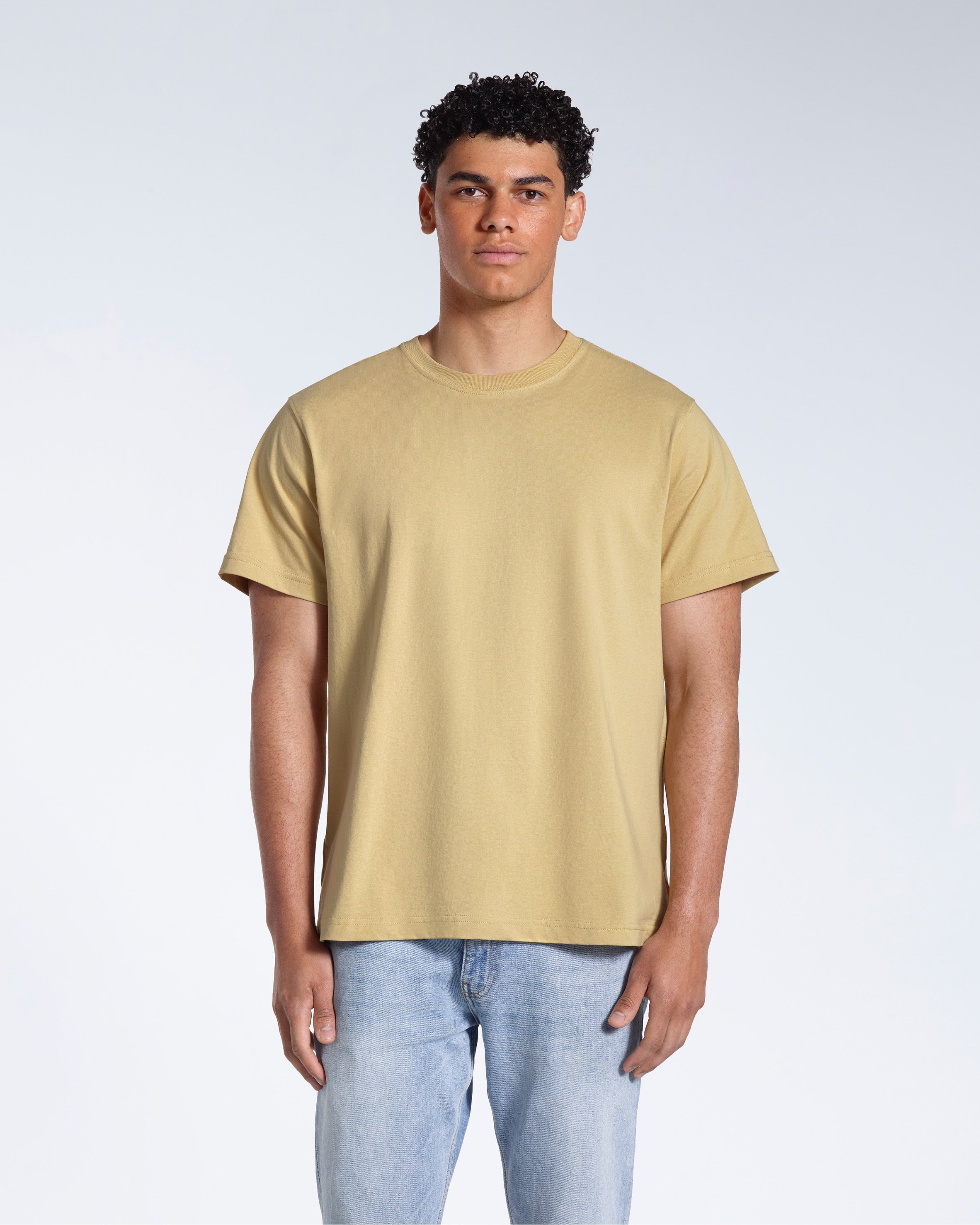 A man facing front on looking into the camera, modelling a plain light khaki short sleeve organic cotton t shirt.