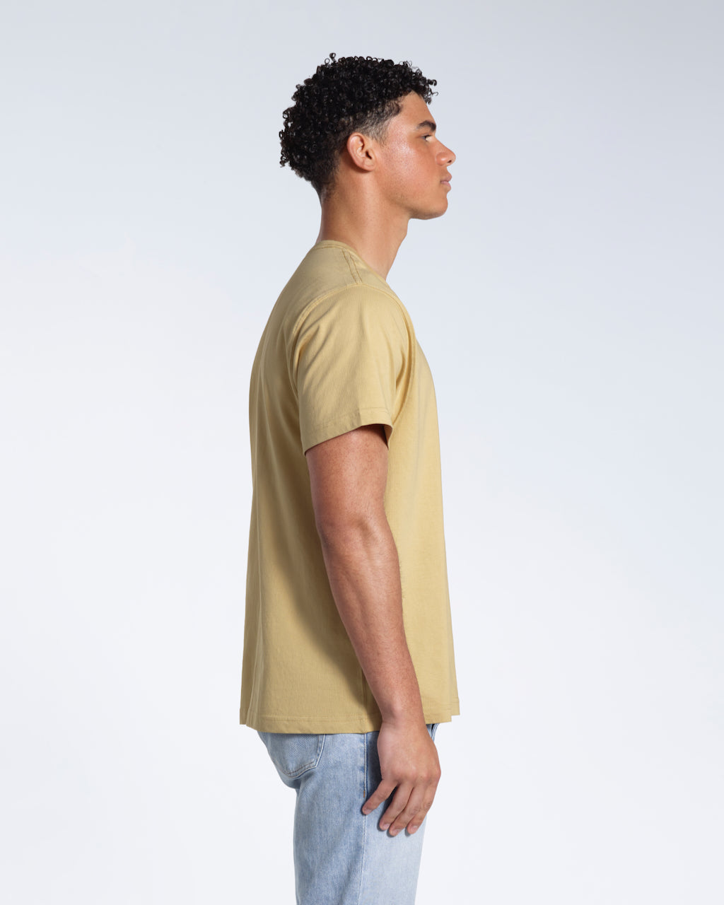 A man facing side on, modelling a plain light khaki short sleeve organic cotton t shirt.