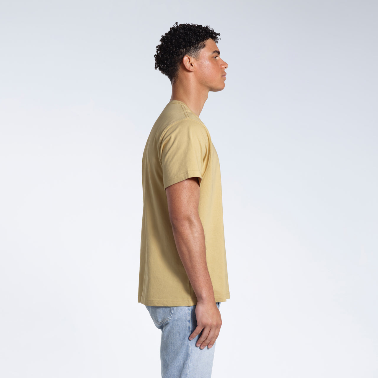A man facing side on, modelling a plain light khaki short sleeve organic cotton t shirt.
