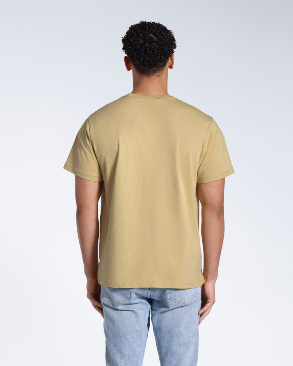 A man facing away from the camera, modelling a plain light khaki short sleeve organic cotton t shirt.
