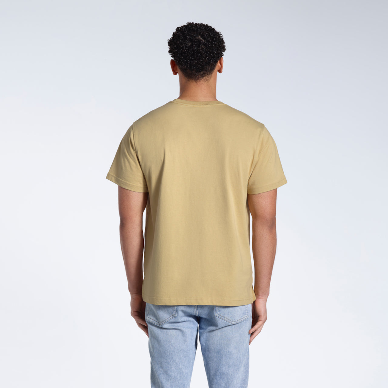 A man facing away from the camera, modelling a plain light khaki short sleeve organic cotton t shirt.