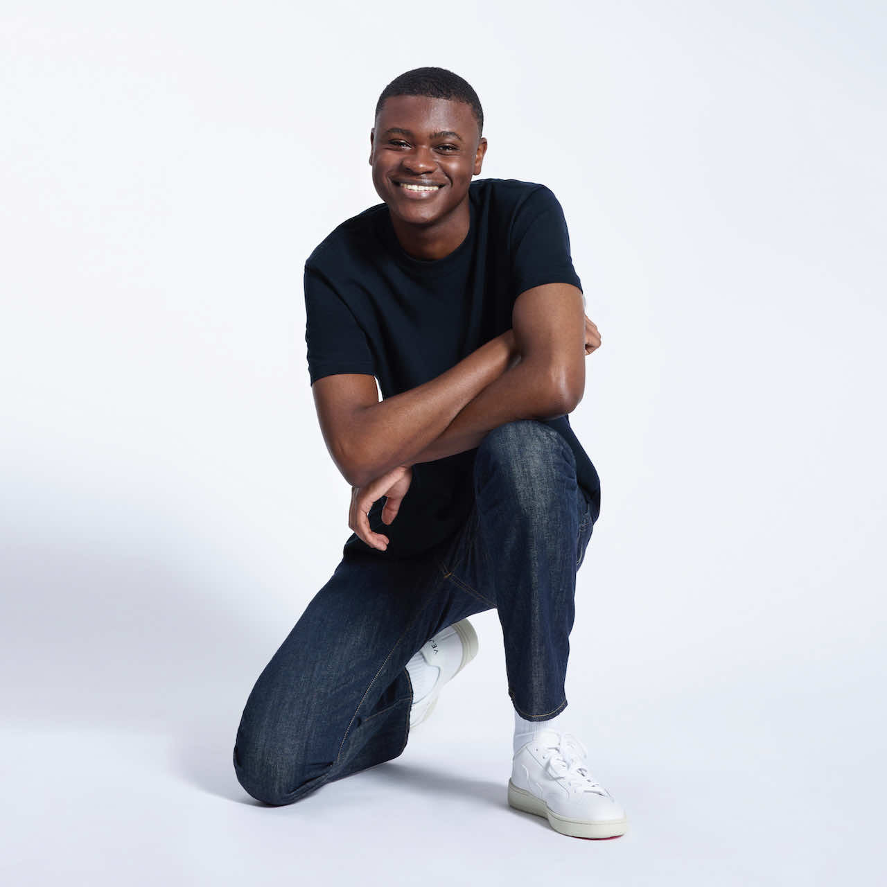 A man kneeling down smiling, modelling a plain navy short sleeve organic cotton t shirt.