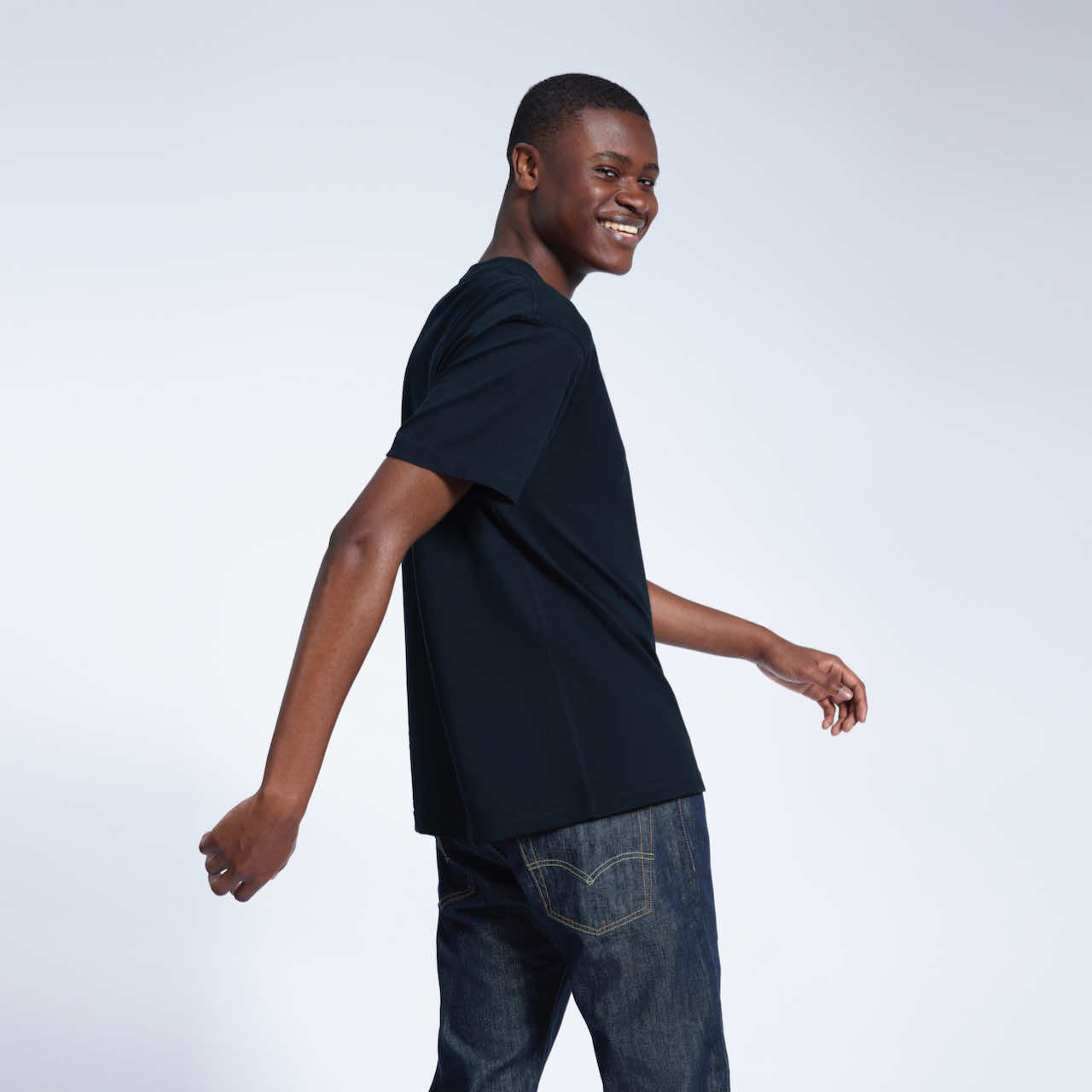 A man looking back smiling, modelling a plain navy short sleeve organic cotton t shirt.