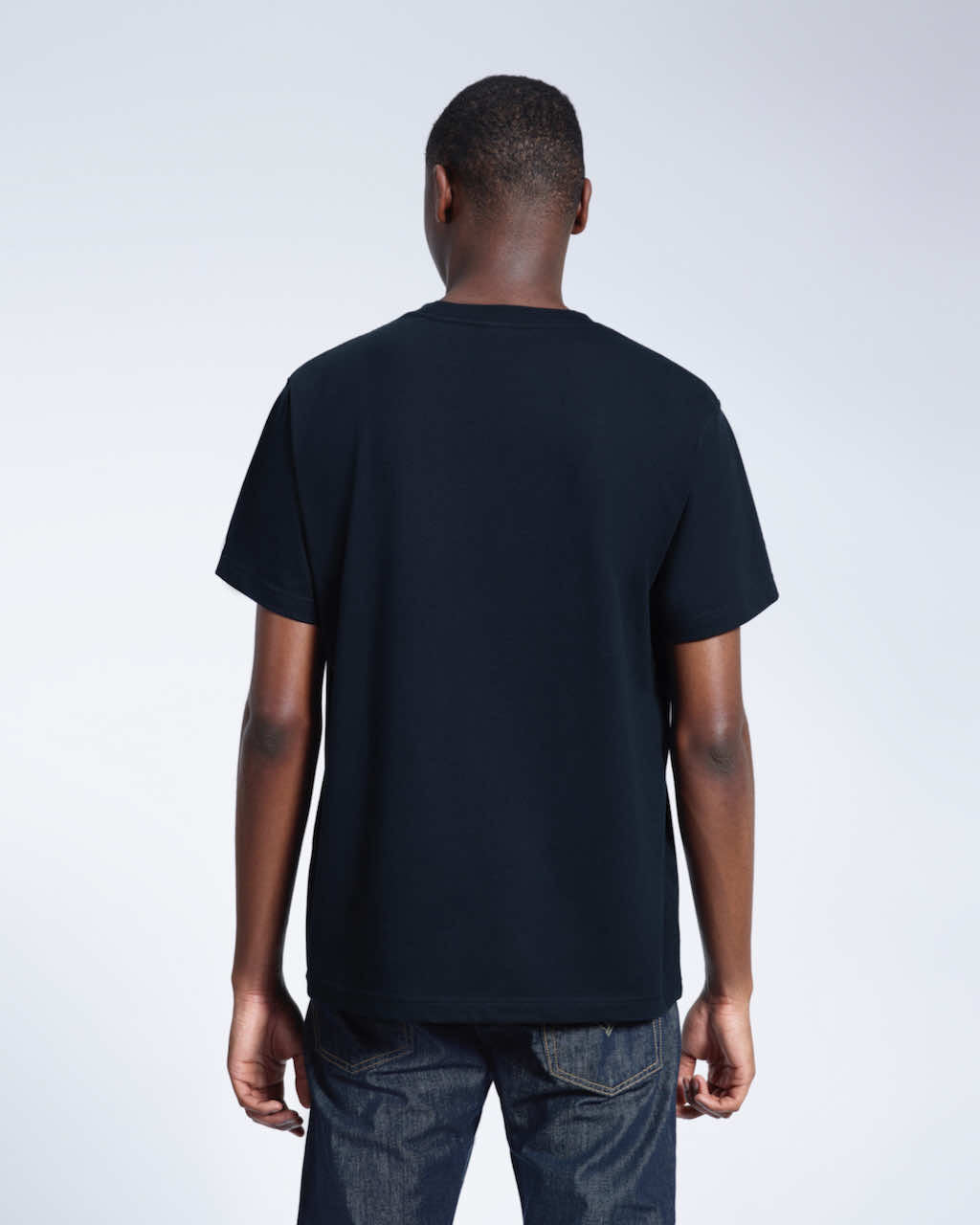 A man facing away from the camera, modelling a plain navy short sleeve organic cotton t shirt.
