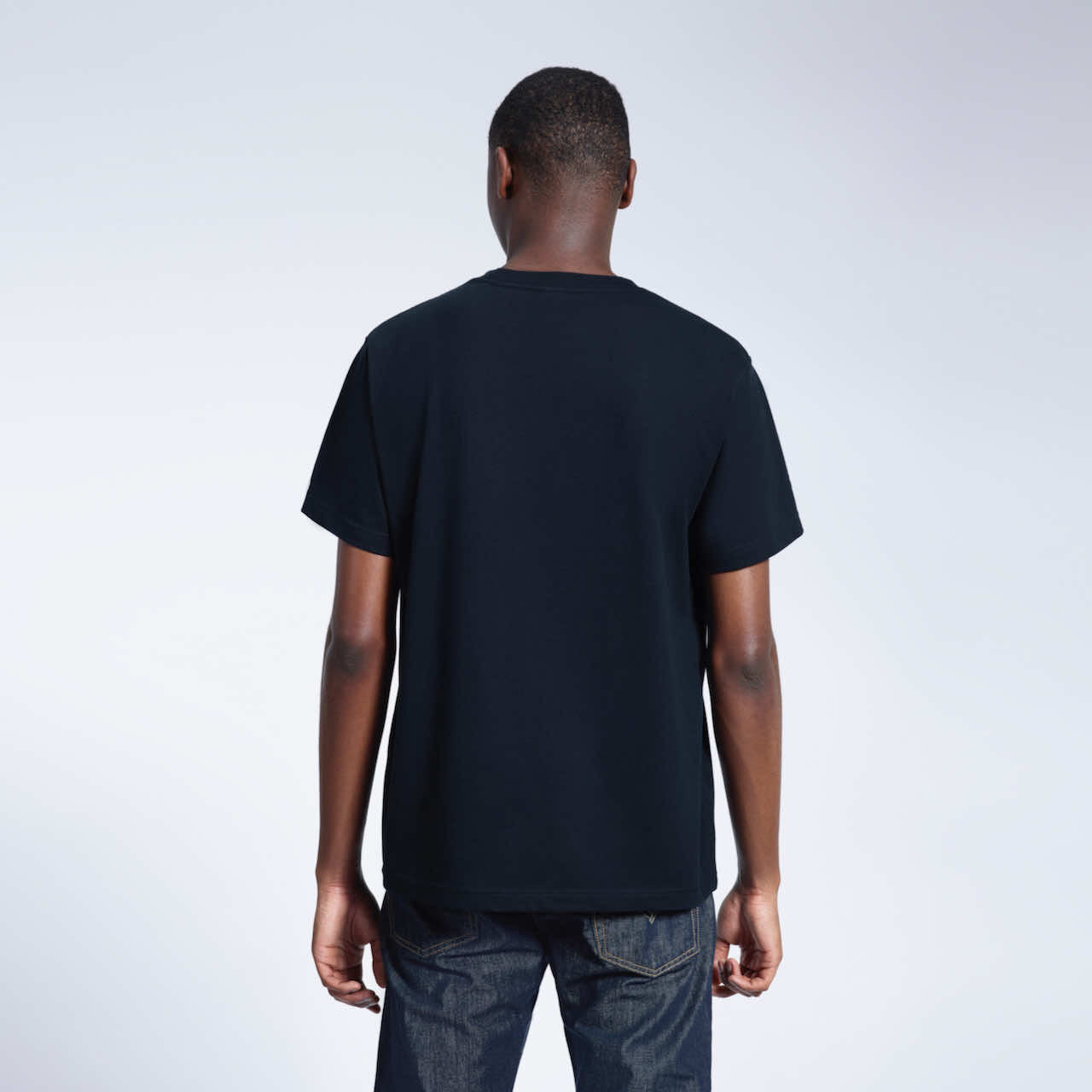 A man facing away from the camera, modelling a plain navy short sleeve organic cotton t shirt.
