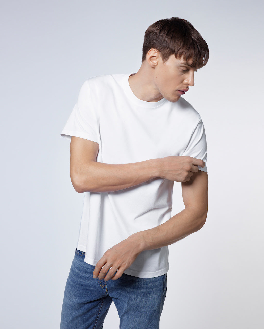 A man looking to the side and touching his sleeve, modelling a plain white short sleeve organic cotton t shirt.