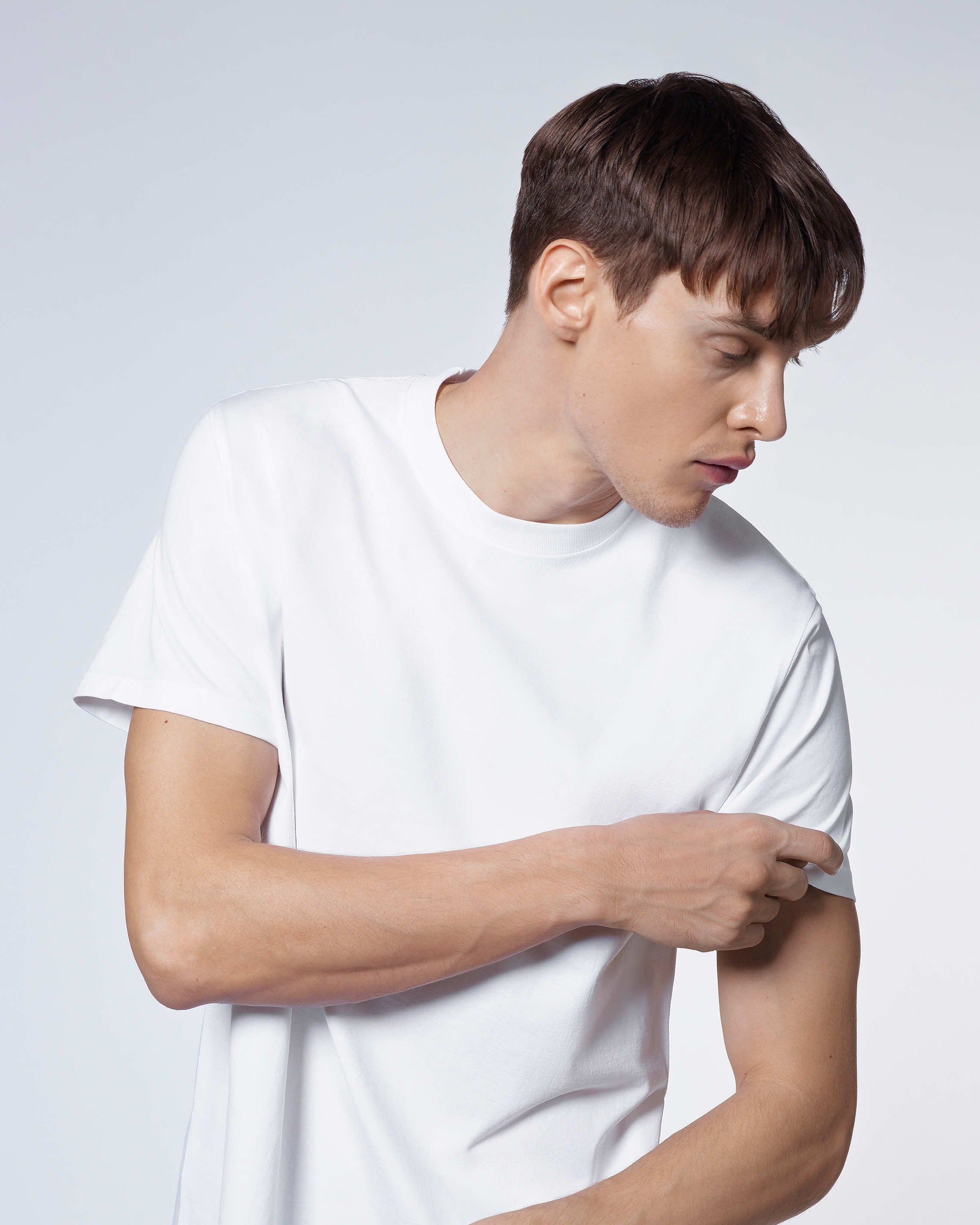 A man looking to the side and touching his sleeve, modelling a plain white short sleeve organic cotton t shirt.