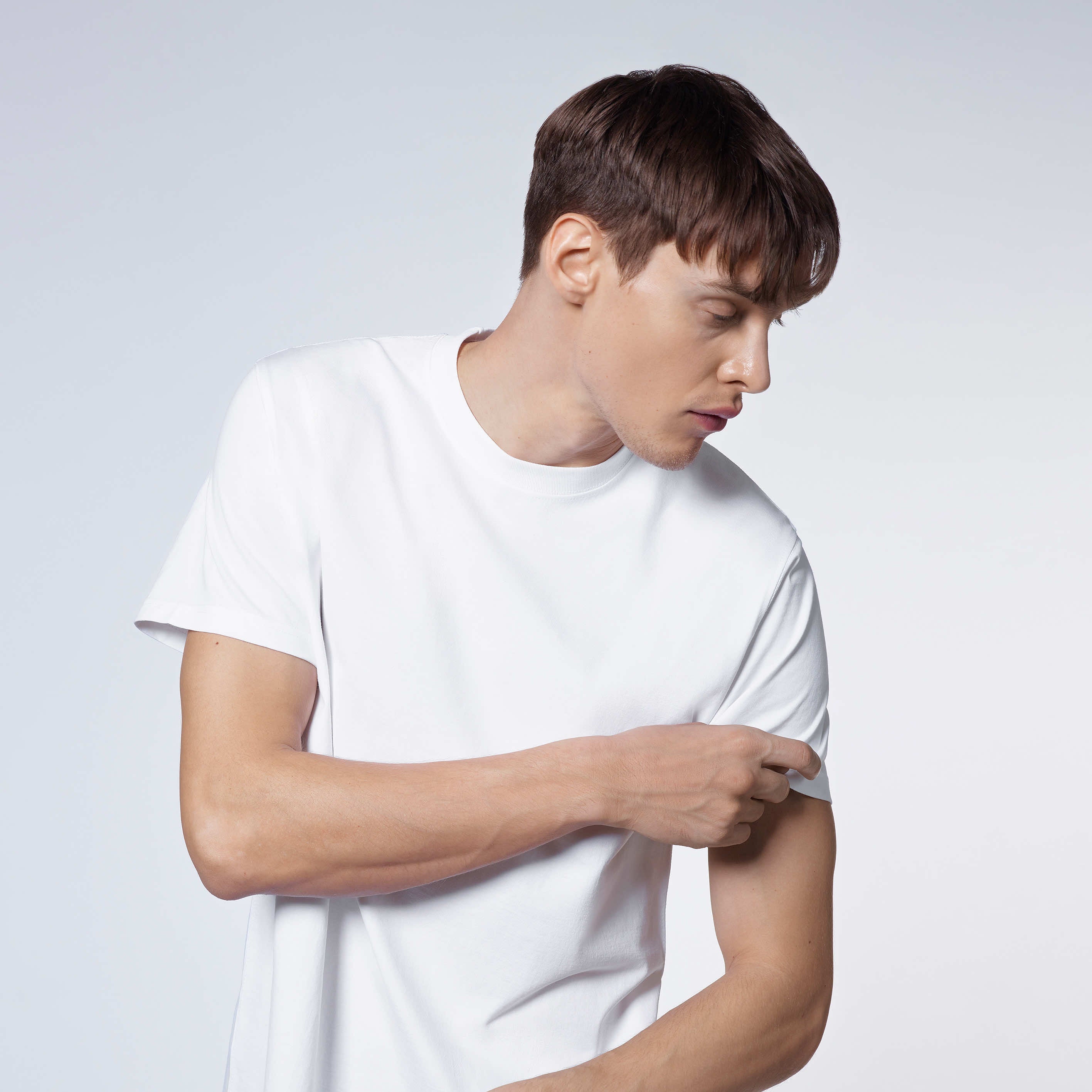A man looking to the side and touching his sleeve, modelling a plain white short sleeve organic cotton t shirt.