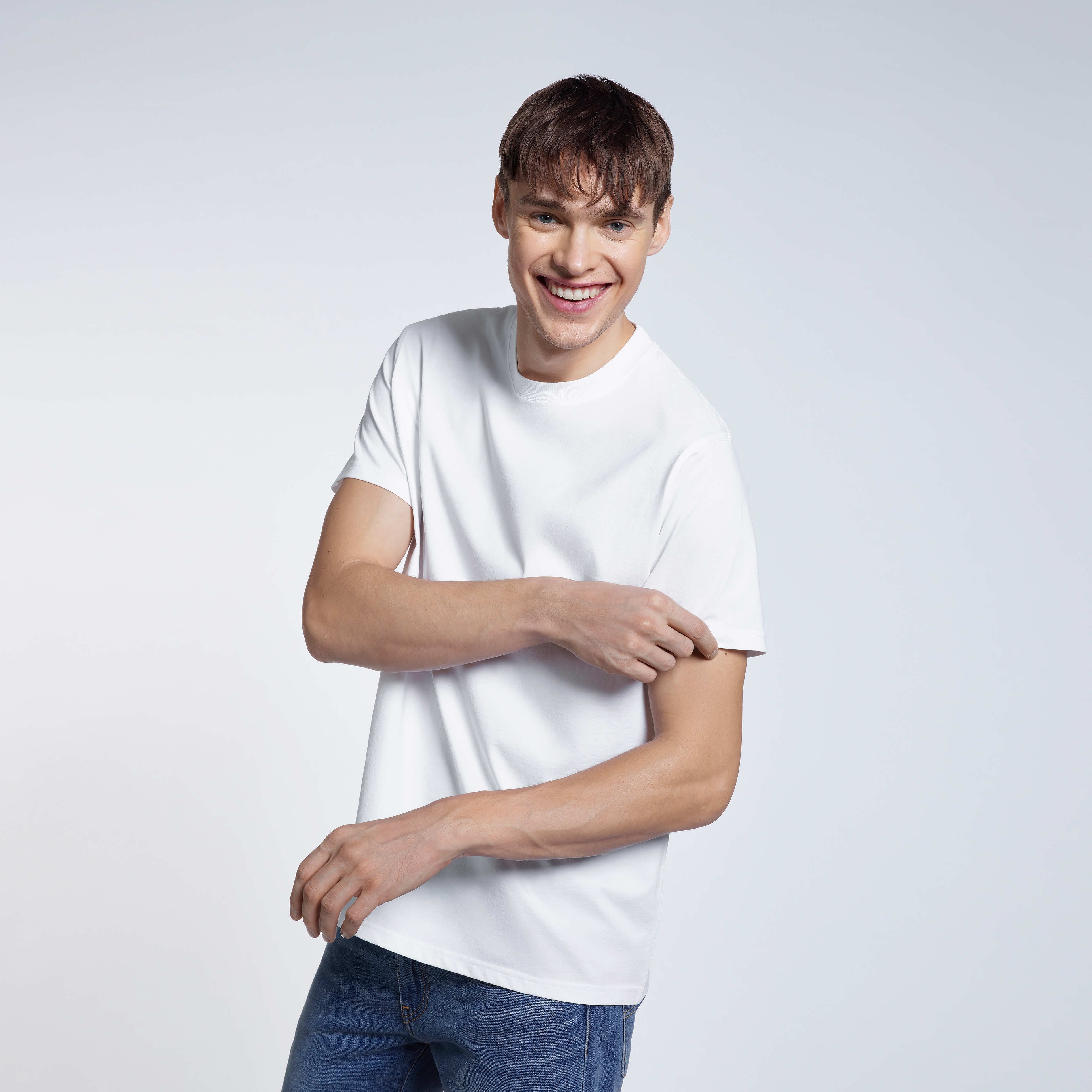 A man smiling touching his sleeve, modelling a plain white short sleeve organic cotton t shirt.