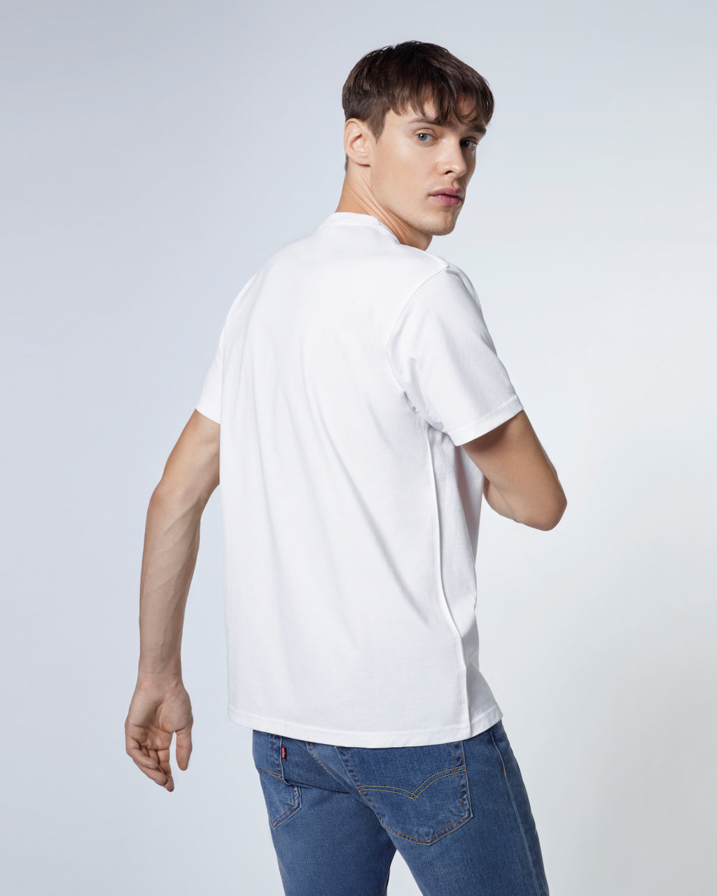 A man looking back towards the camera, modelling a plain white short sleeve organic cotton t shirt.