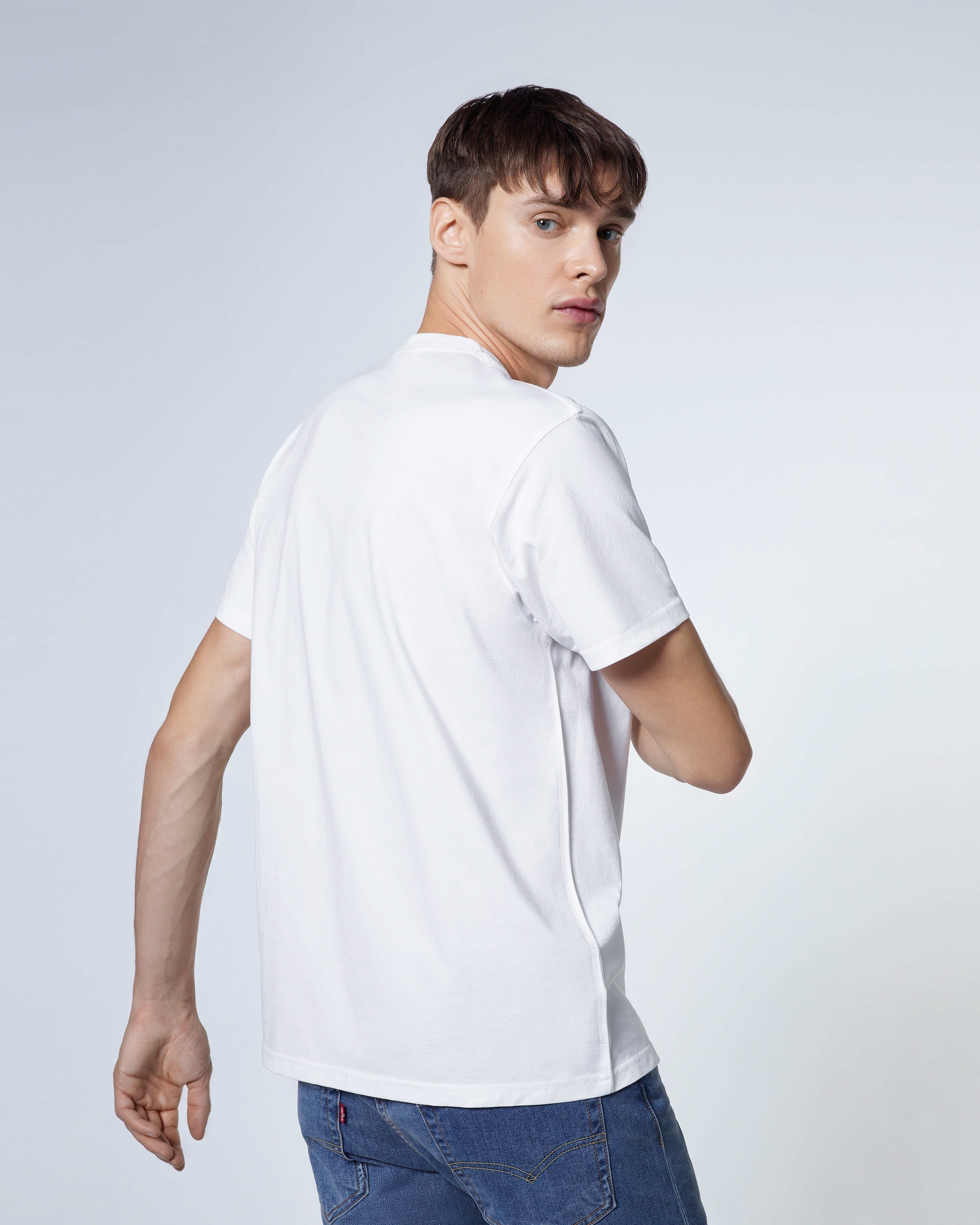 A man looking back towards the camera, modelling a plain white short sleeve organic cotton t shirt.