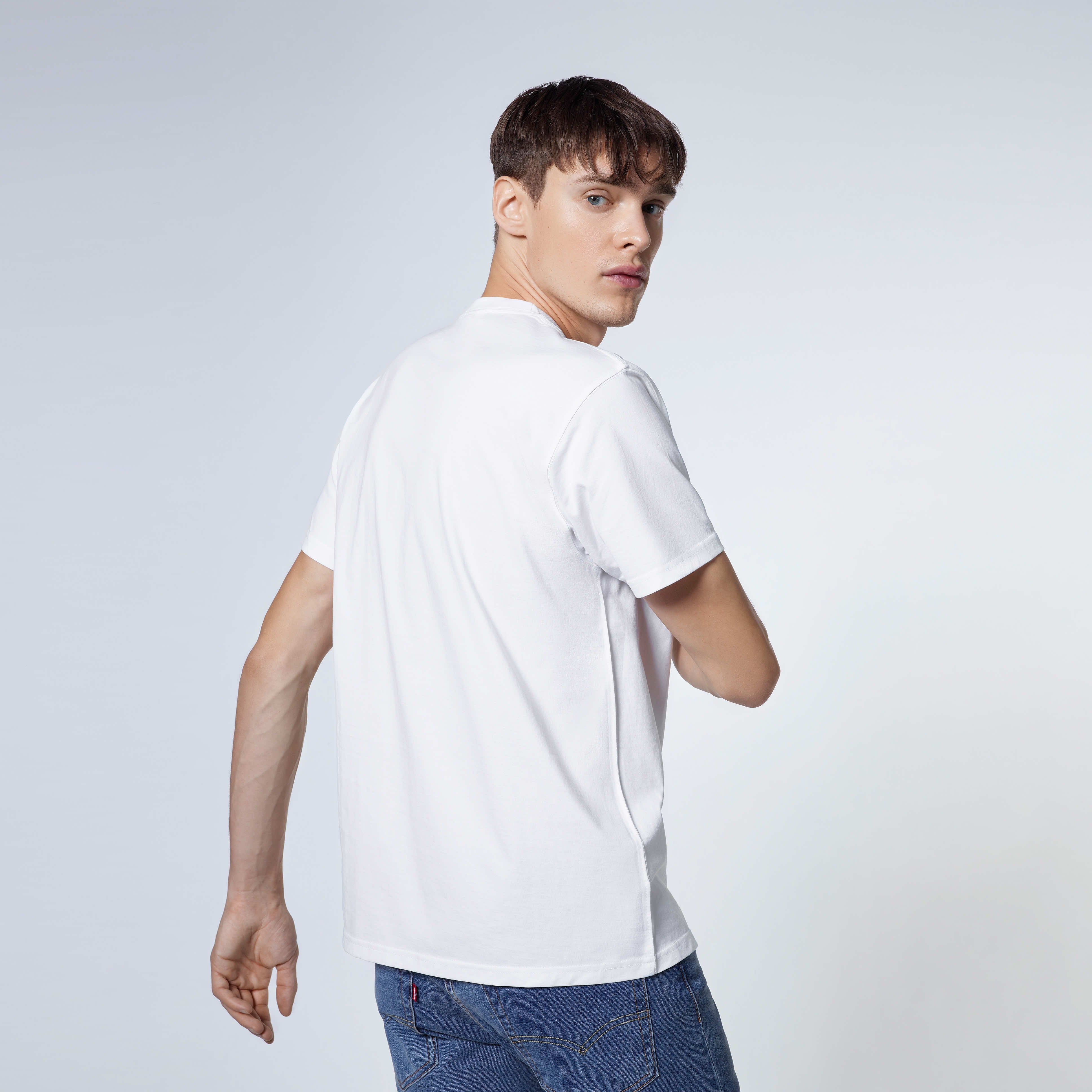 A man looking back towards the camera, modelling a plain white short sleeve organic cotton t shirt.