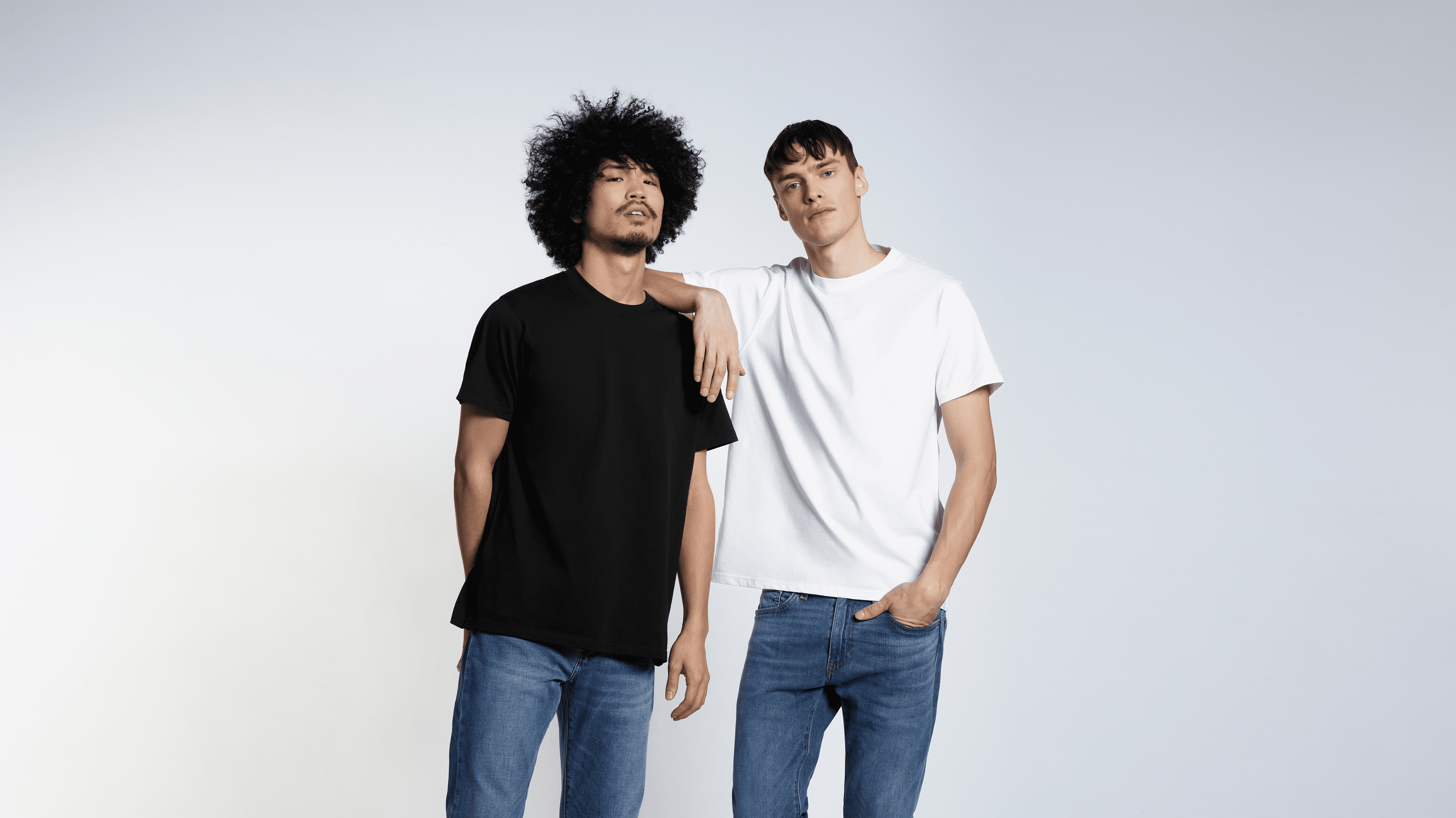 Two men looking into the camera, modelling plain black and white organic cotton t shirts.