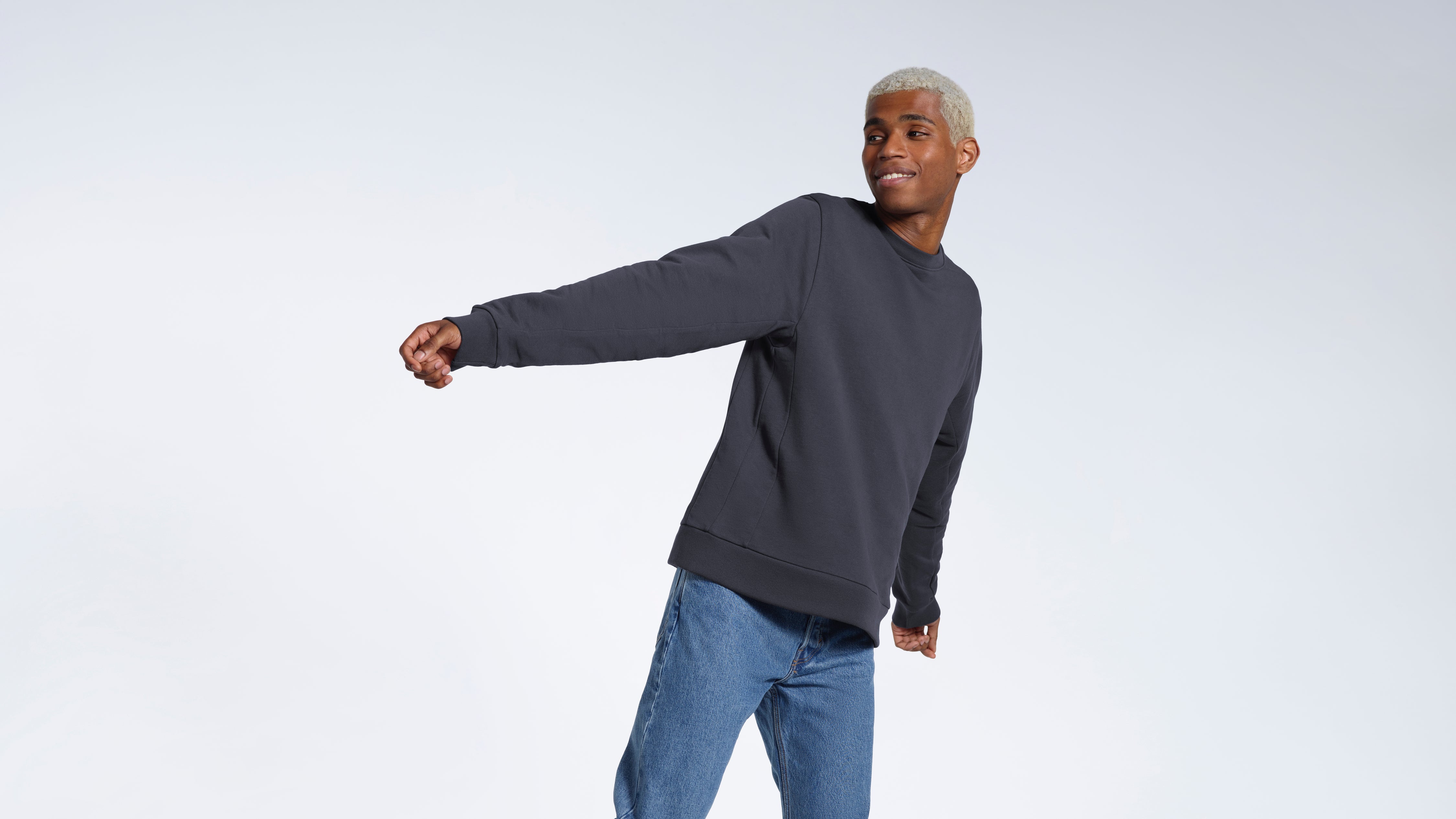 A man smiling looking away from the camera, modelling a plain dark grey french terry organic cotton sweatshirt.
