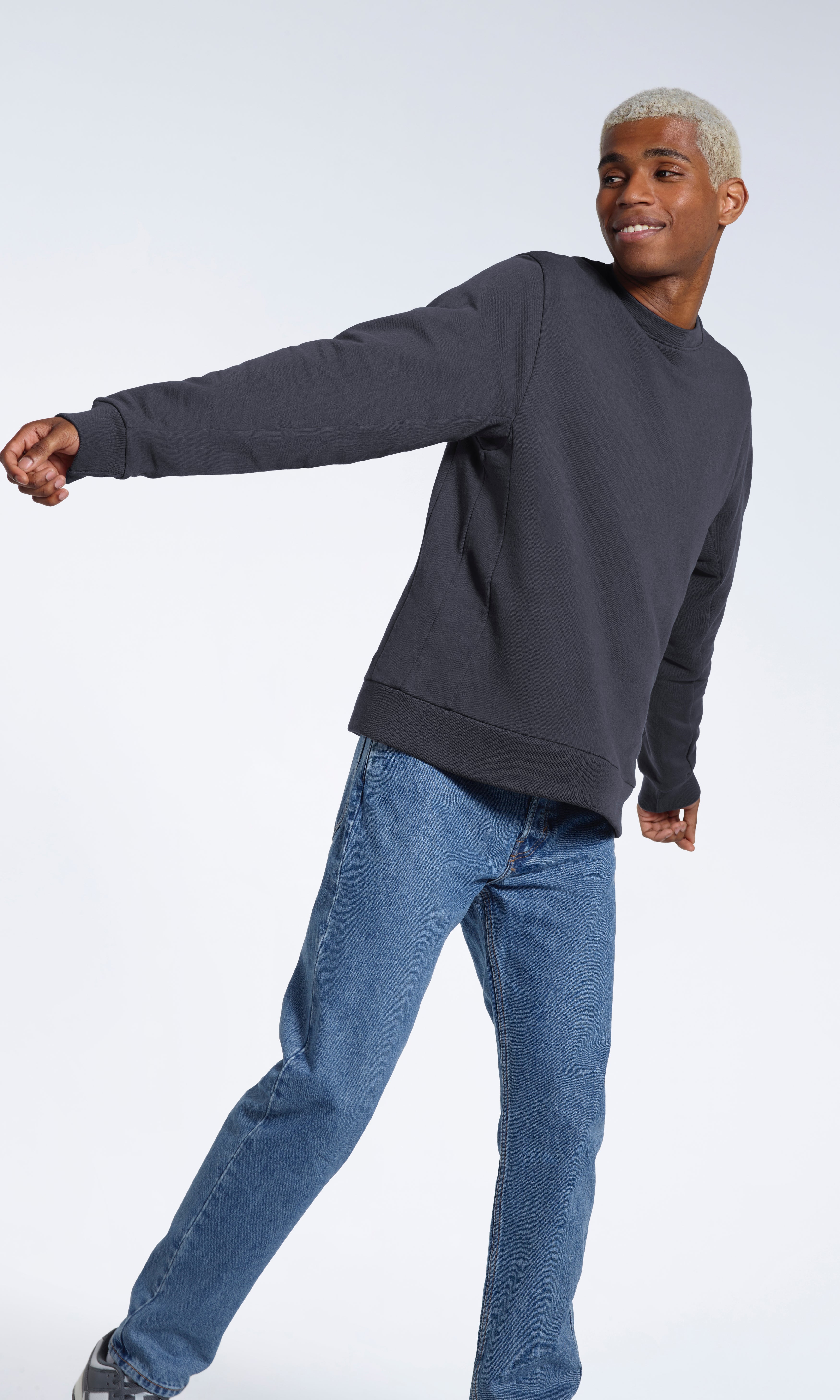 A man smiling looking away from the camera, modelling a plain dark grey french terry organic cotton sweatshirt.