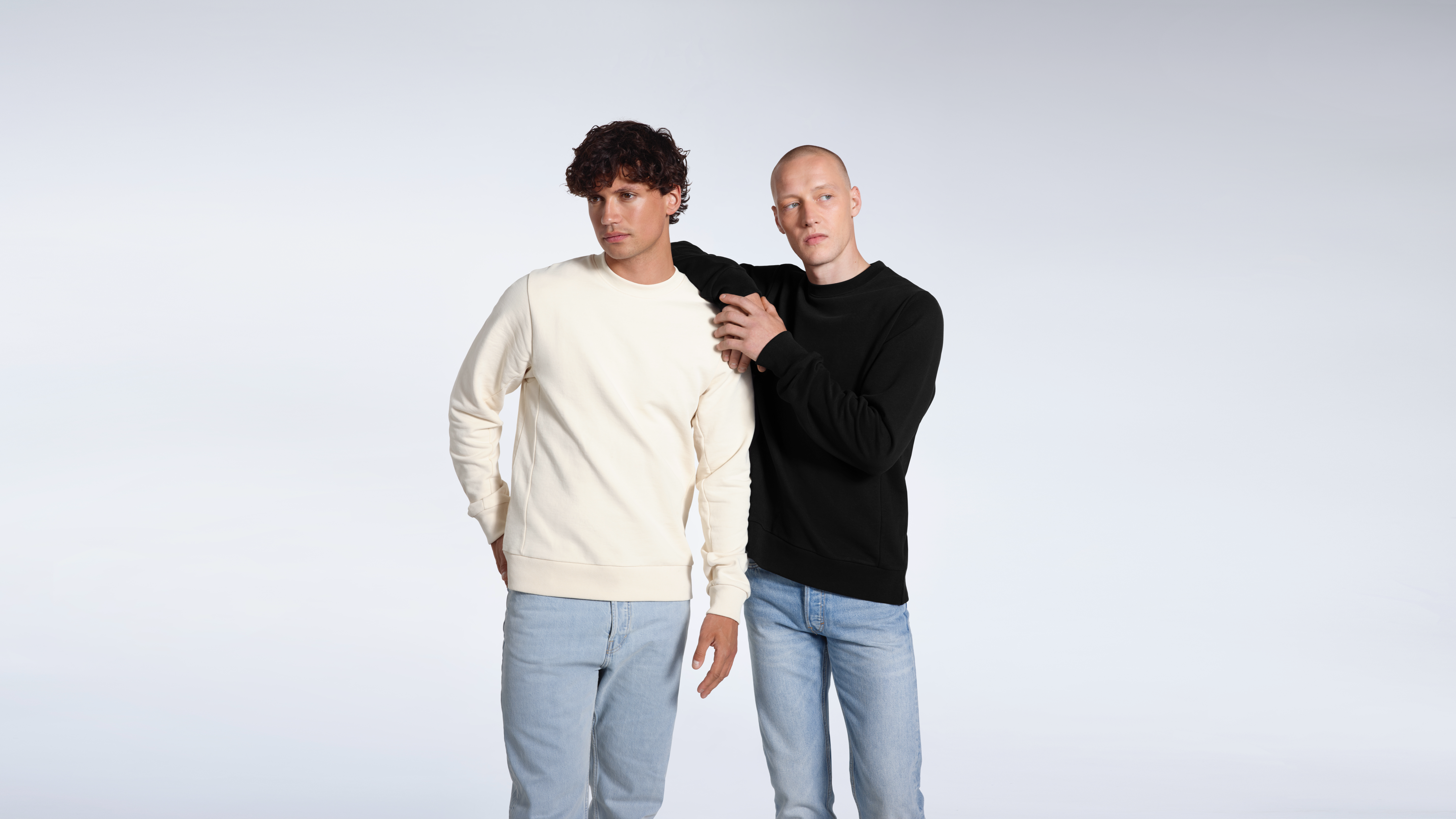 Two men looking away from the camera, modelling plain ecru and black organic cotton sweatshirts.