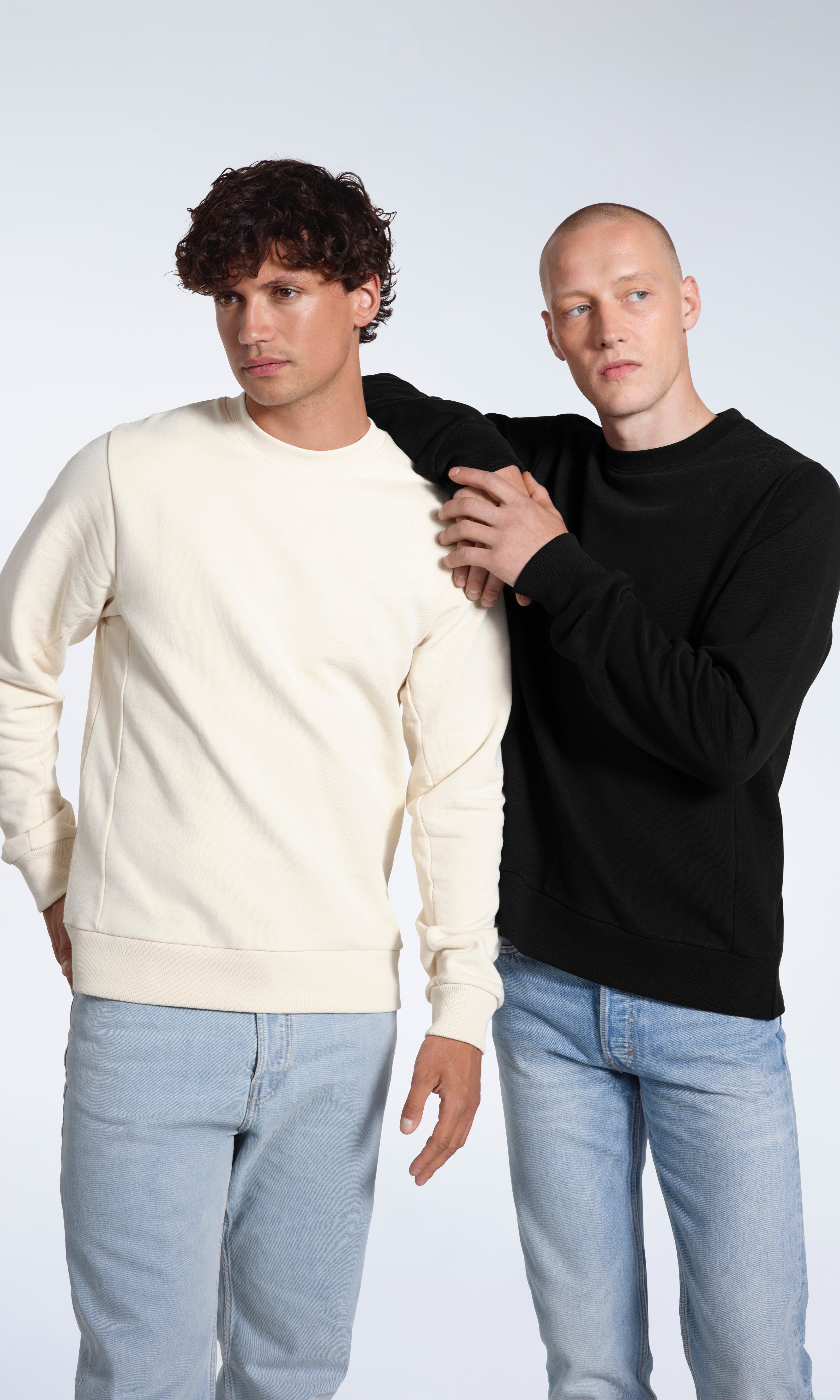 Two men looking away from the camera, modelling plain ecru and black organic cotton sweatshirts.